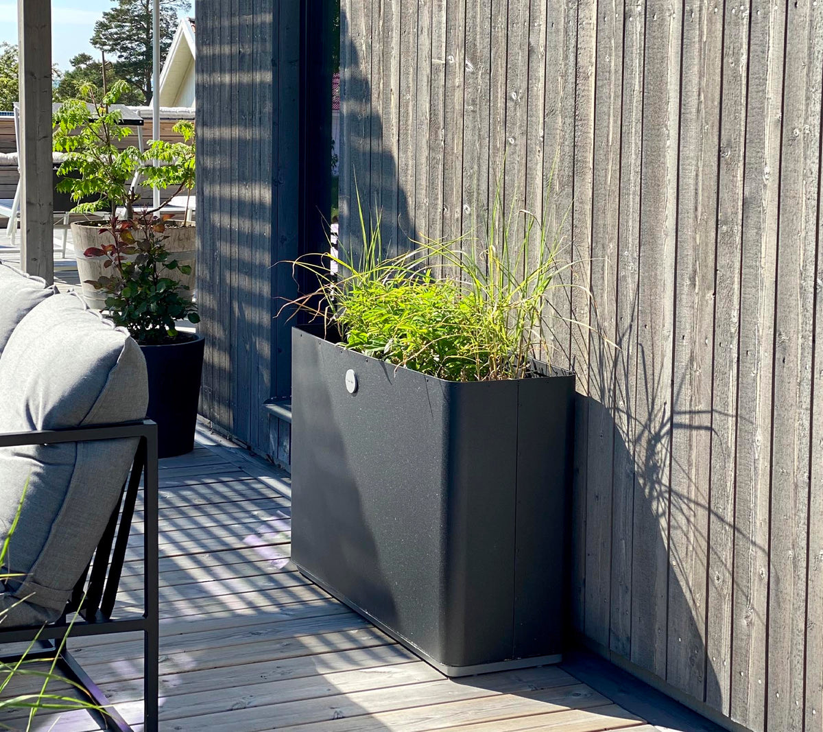 Een strakke, moderne plantenbak met levendige groene planten staat tegen een gestructureerde houten muur en complementair aan de omliggende ruimte.