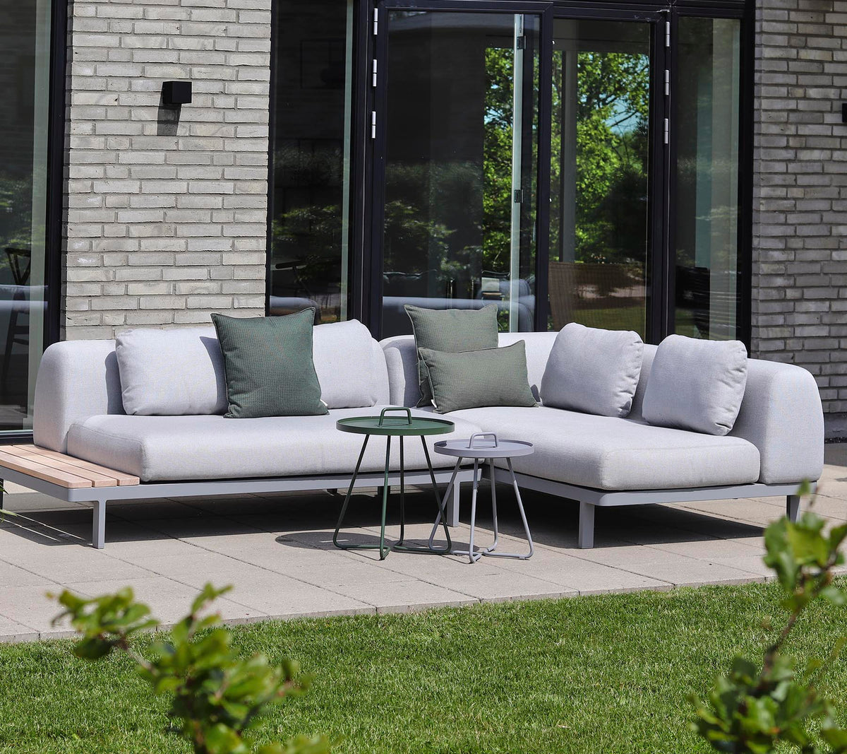 Moderne sectionele bank in lichte stof met decoratieve kussens, gecombineerd met kleine bijzettafels in een rustige setting.