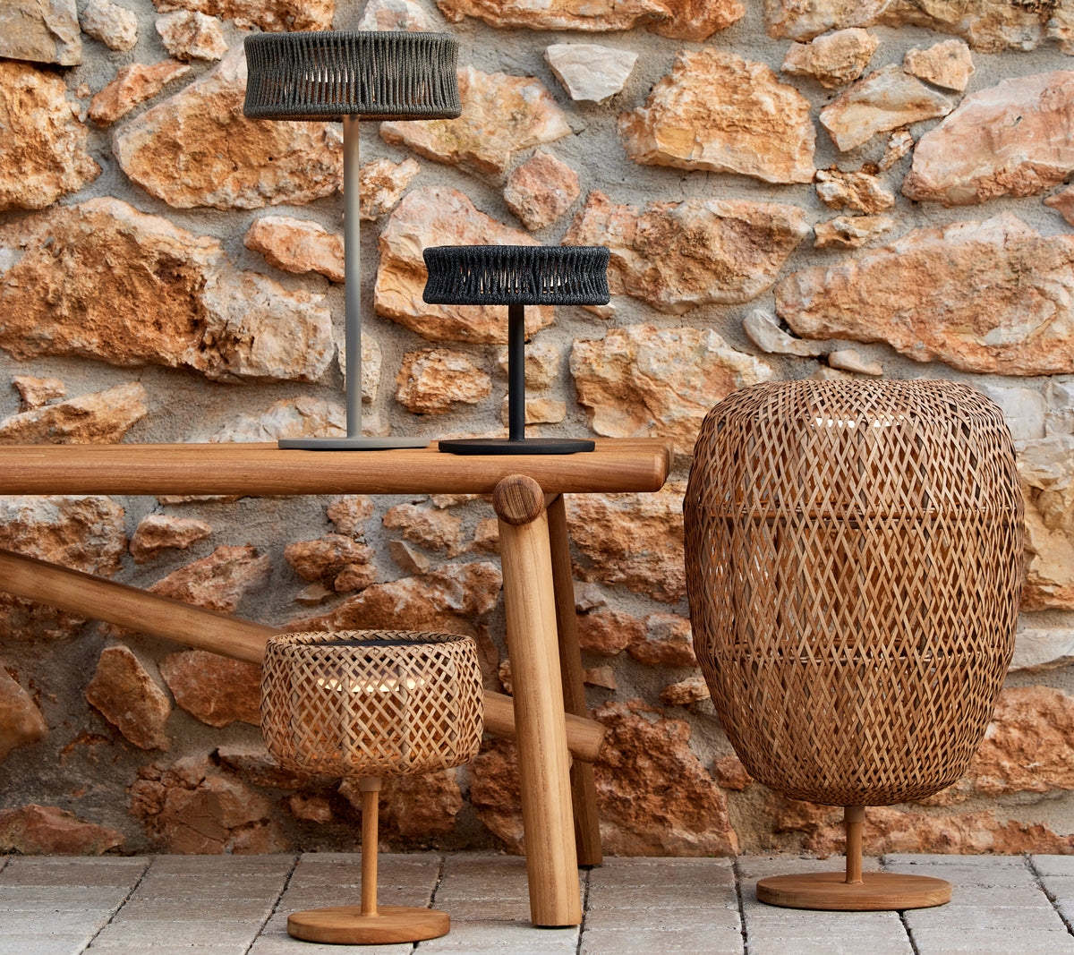 Drie decoratieve lampen in verschillende vormen en maten op een houten tafel, tegen een gestructureerde stenen muur.