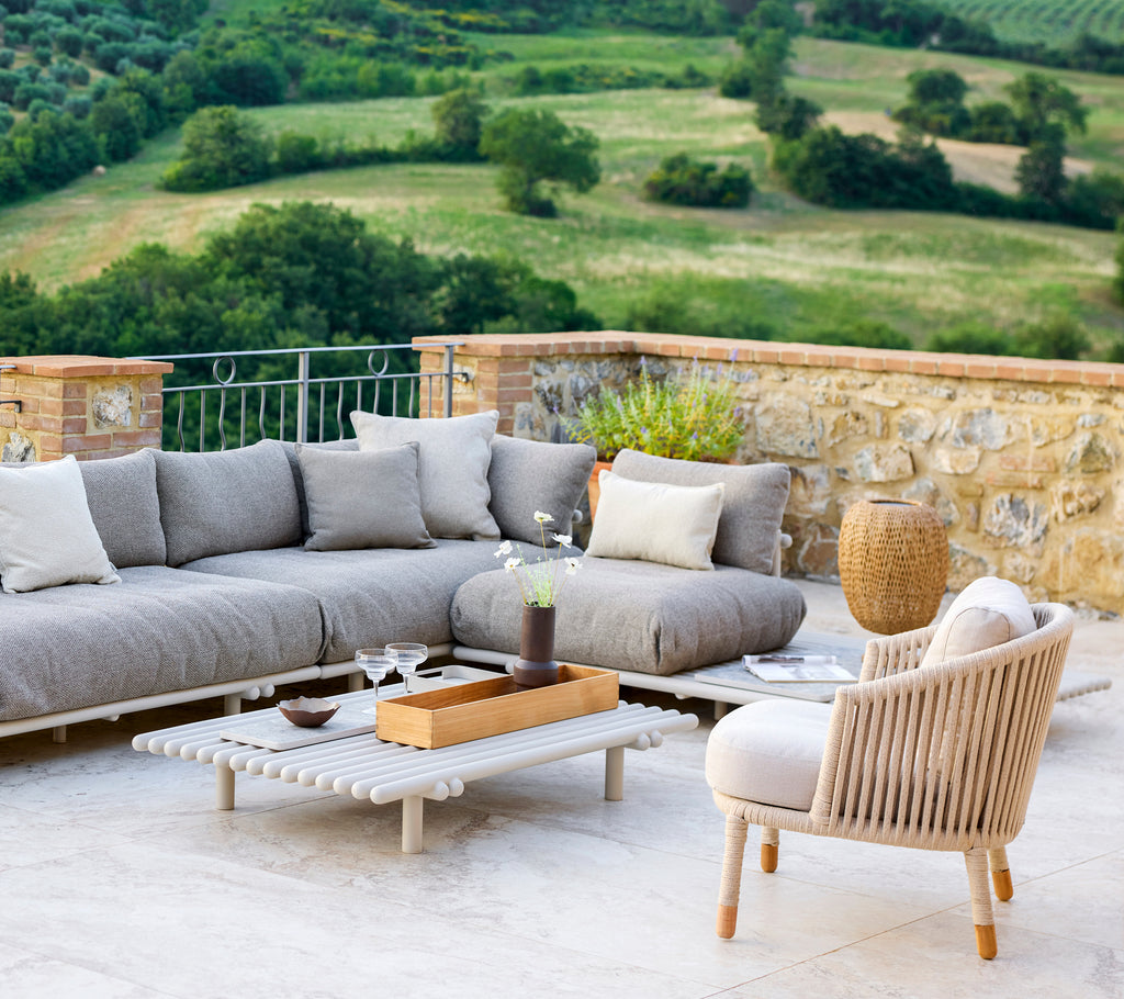 Stijlvolle lounge-opstelling met een comfortabele hoekbank, een lichte accentstoel en moderne decoratie tegen een sereen landschap.