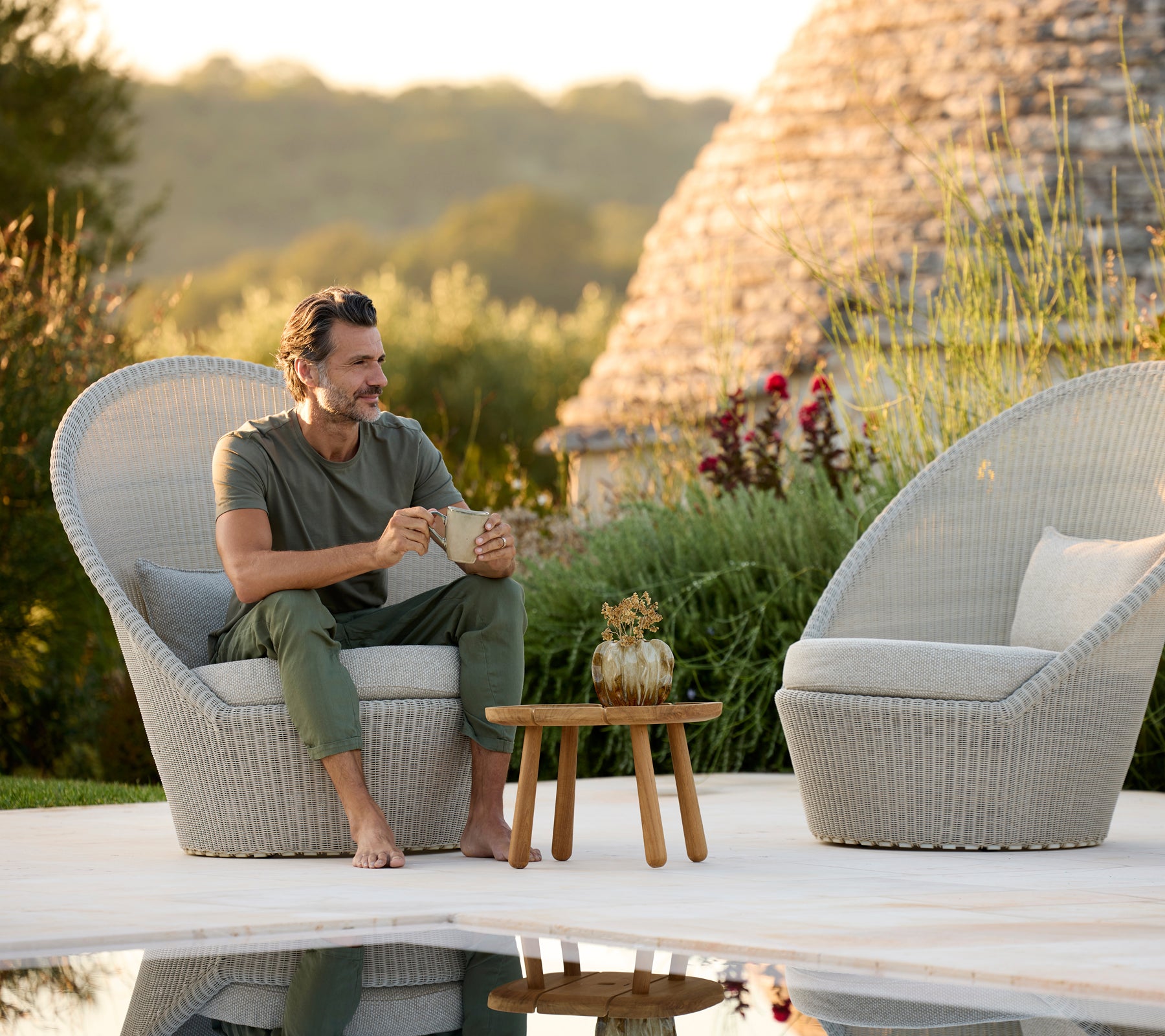 Moderne grijze lounge stoelen met een houten tafel naast een zwembad.