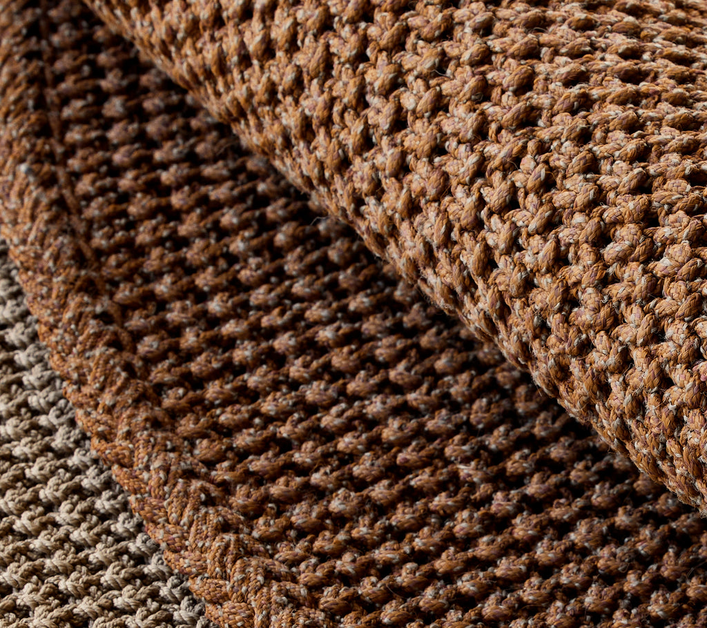 Close-up van een textuurgebroken brei tapijt, dat rijke bruintinten en complexe weefpatronen toont.