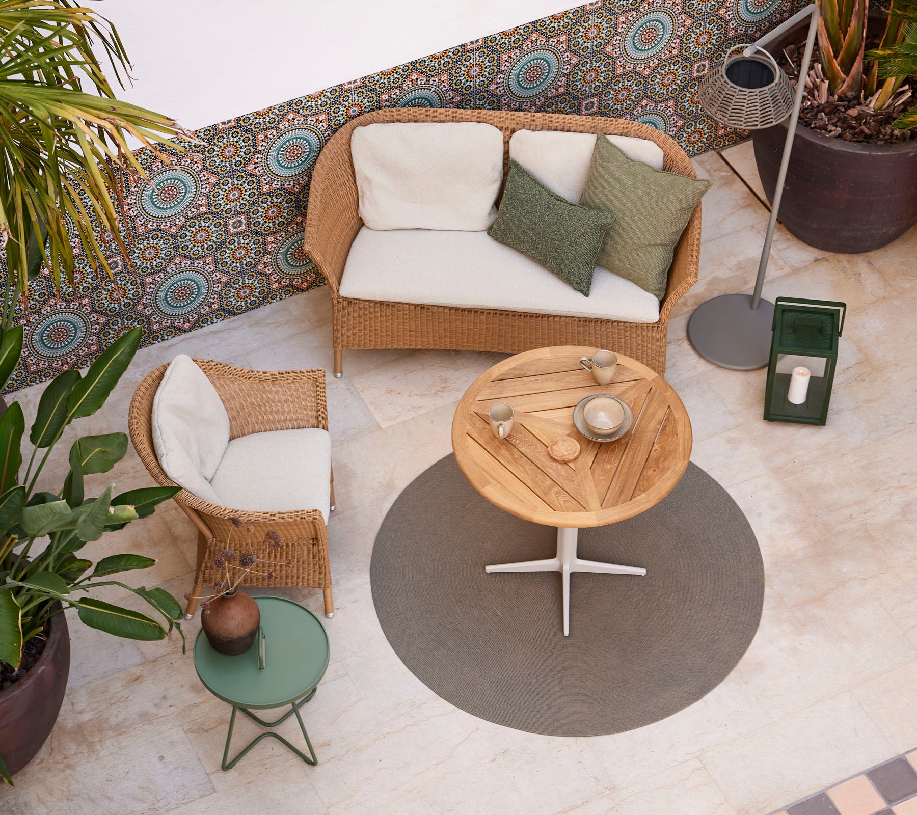 Een gezellige zithoek met een rattan bank, een ronde houten salontafel en potplanten, die een stijlvolle sfeer versterken.