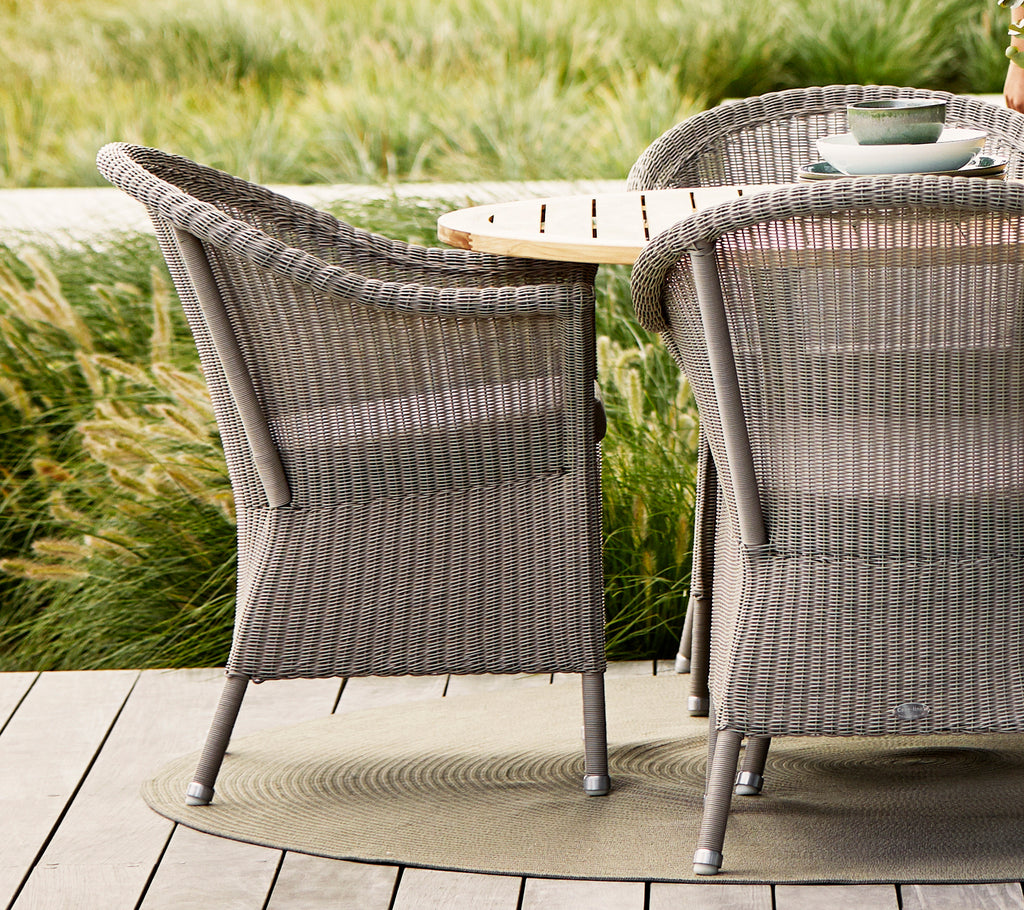 Taupe Lansing-stoelen met gestructureerd geweven design, gecombineerd met een tafel van natuurlijk hout en omringd door weelderig groen.