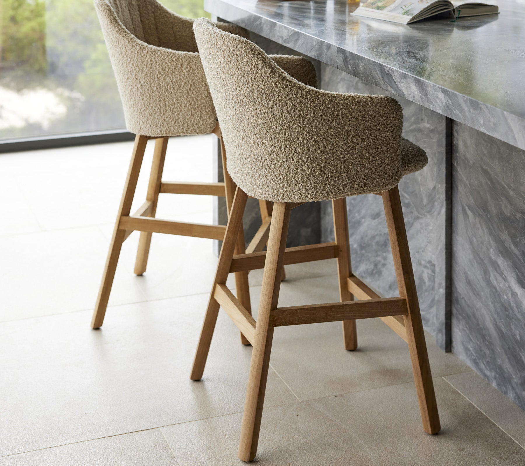 Twee moderne barstoelen met gevoerde zittingen en houten poten, gelegen bij een elegante marmeren bar.