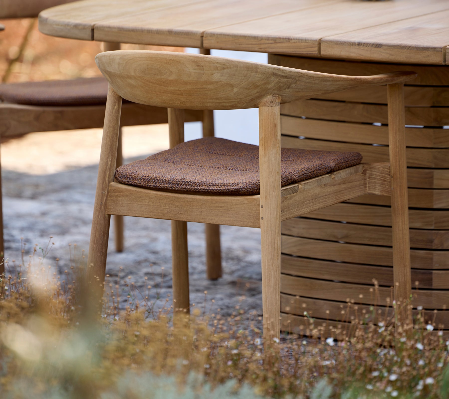 Houten stoel met bruine kussen naast een ronde tafel in een buitenomgeving.