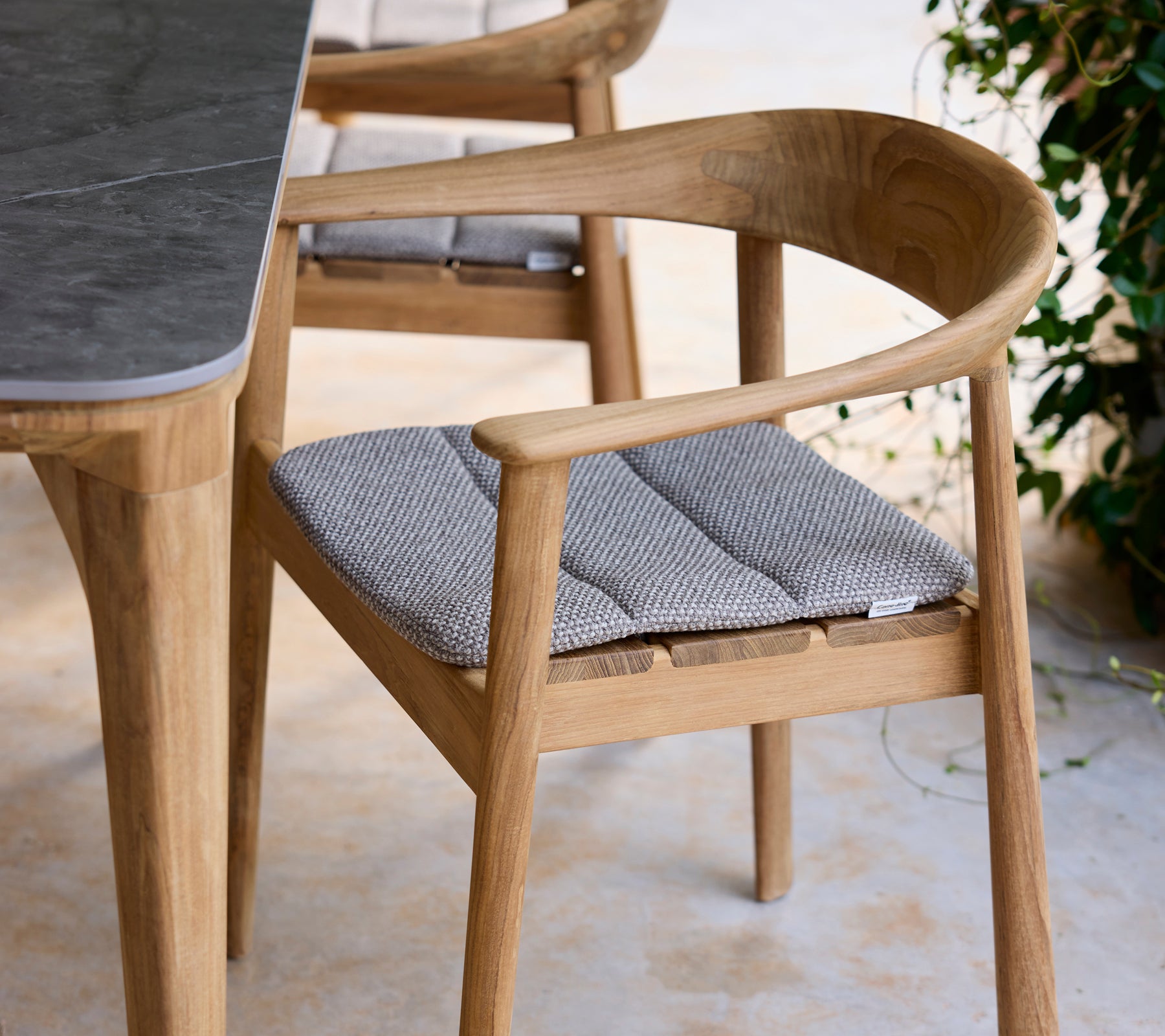 Moderne houten stoel met grijze kussen naast een tafel in een lounge-setting.