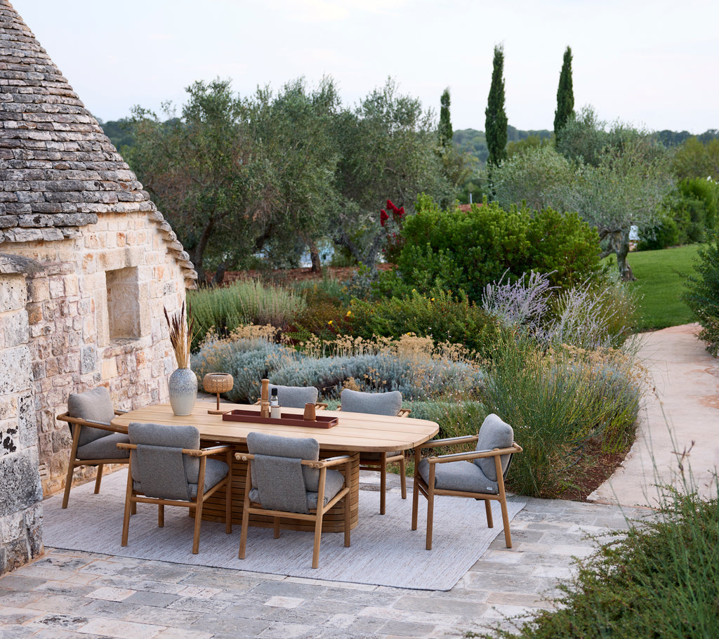 Moderne buitentuinset met een ronde tafel en grijze stoelen omgeven door groen.