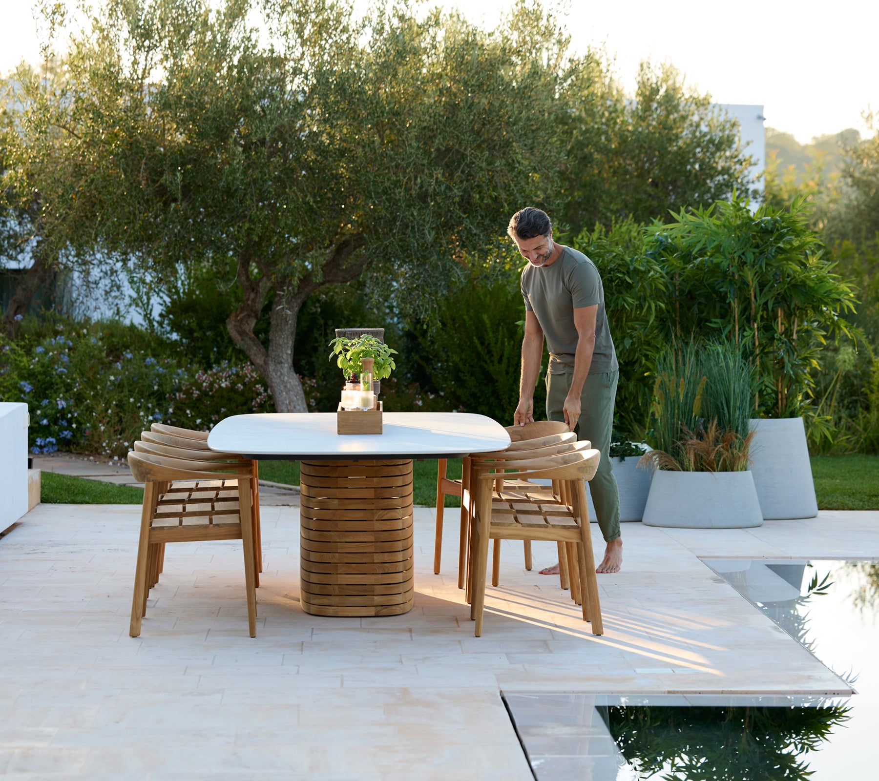 Moderne ronde buitentafel met houten stoelen en groen op de achtergrond.
