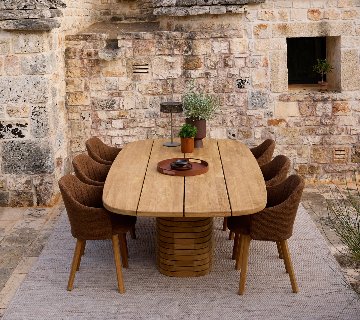 Modern houten eettafel omringd door bruine stoelen in een rustieke setting.