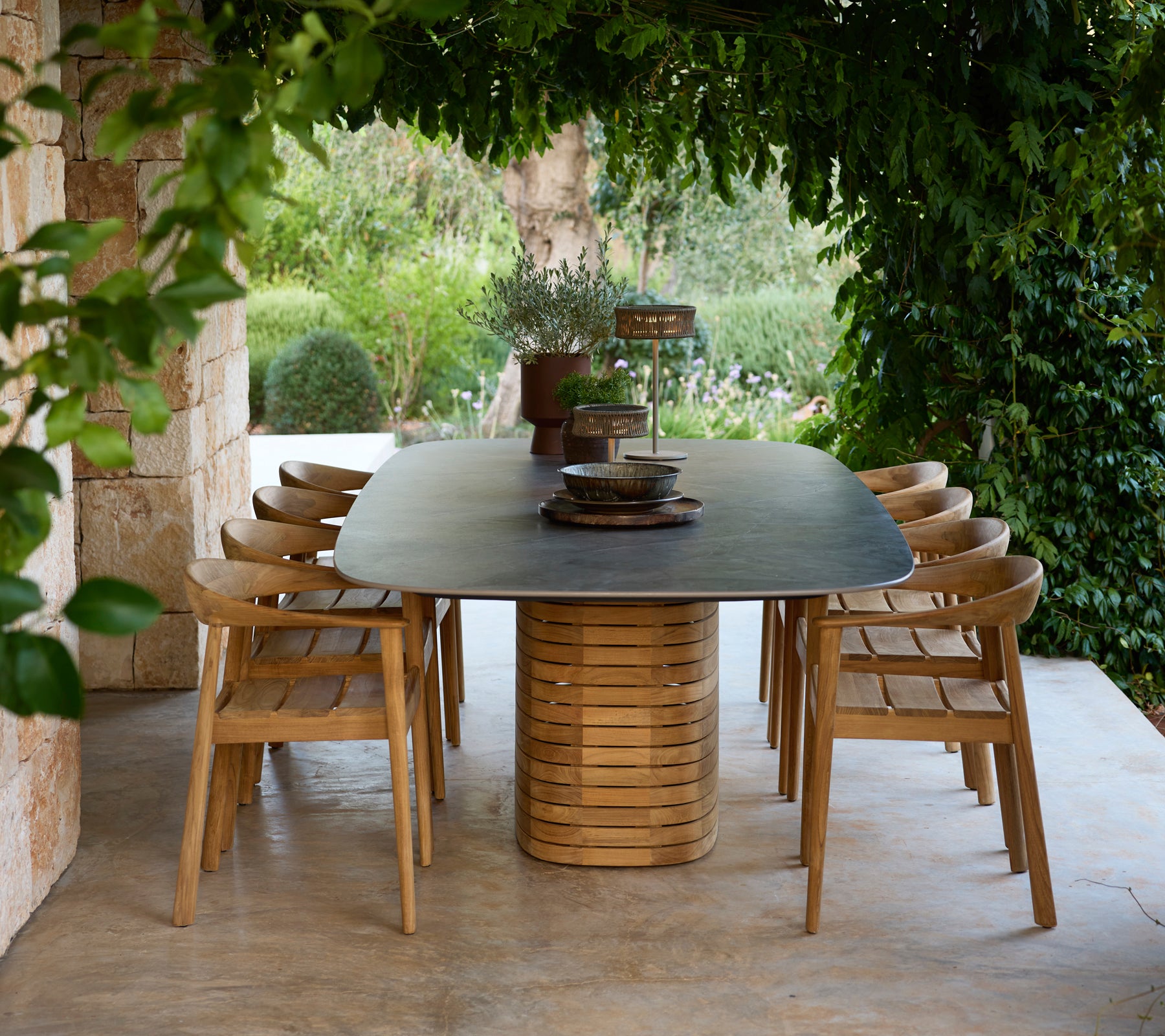 Moderne buitentafel met houten stoelen omringd door groen.