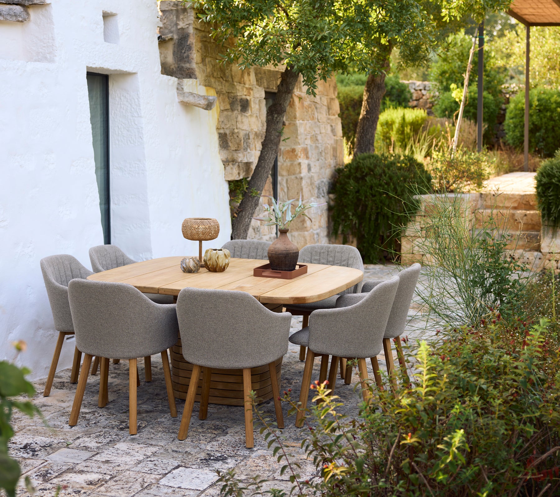 Modern houten eettafel omringd door grijze stoelen in een tuinsetting.