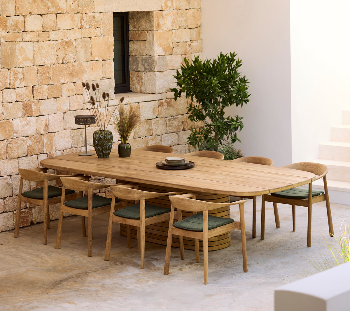 Moderne houten eettafel met groene kussens en houten stoelen in een minimalistische setting.