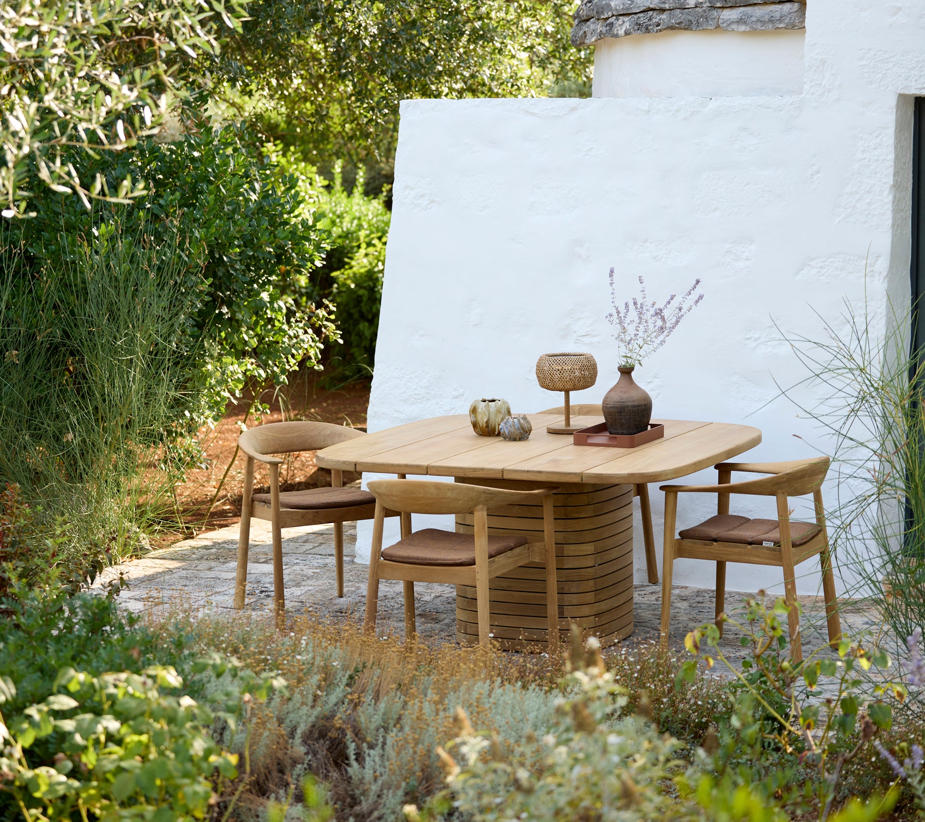 Modern rond tafel met houten stoelen en decoratieve vaas in een buitenomgeving.