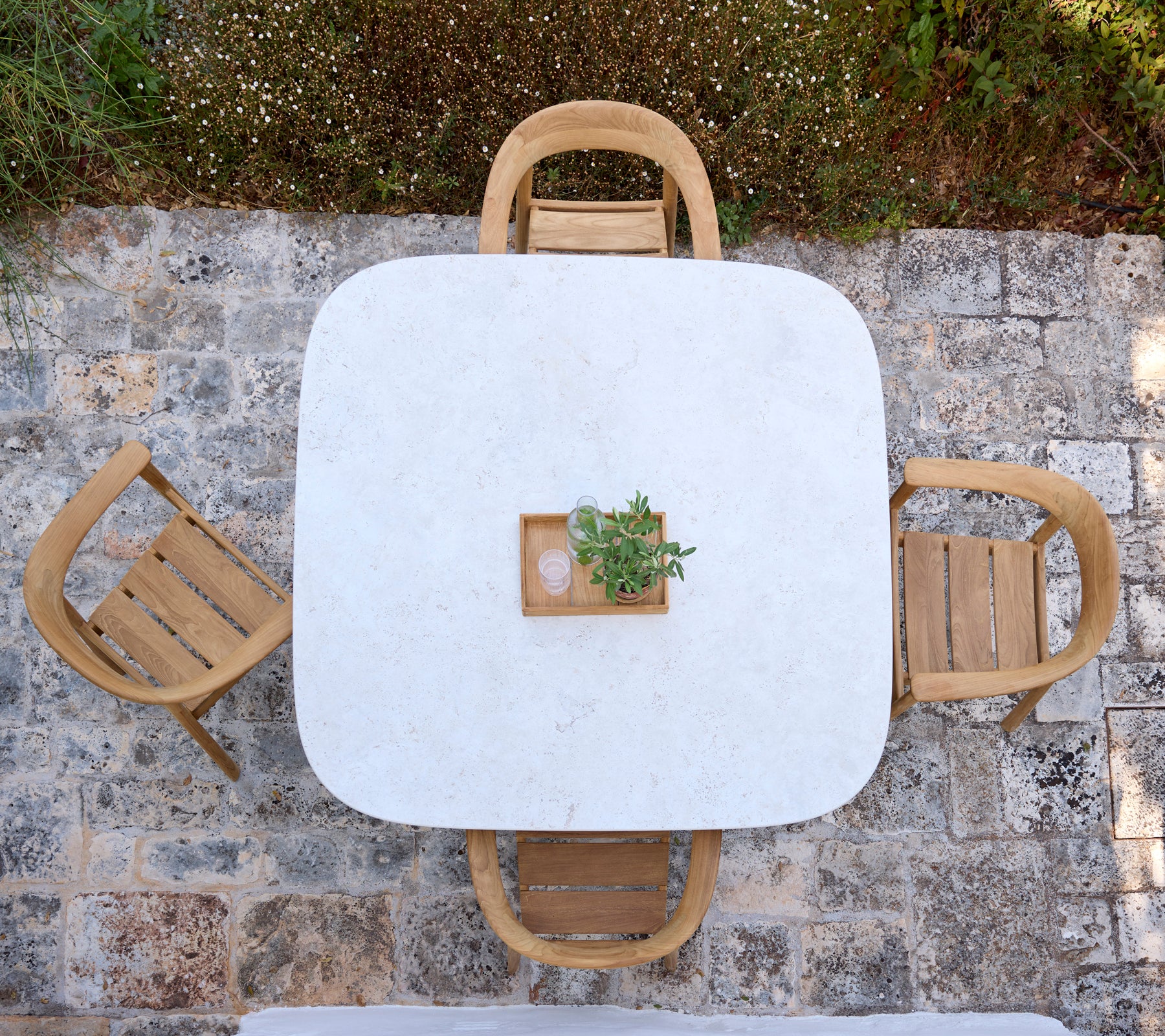 Modern wit tafel met houten stoelen en een klein plantencentrum in een buitenomgeving.