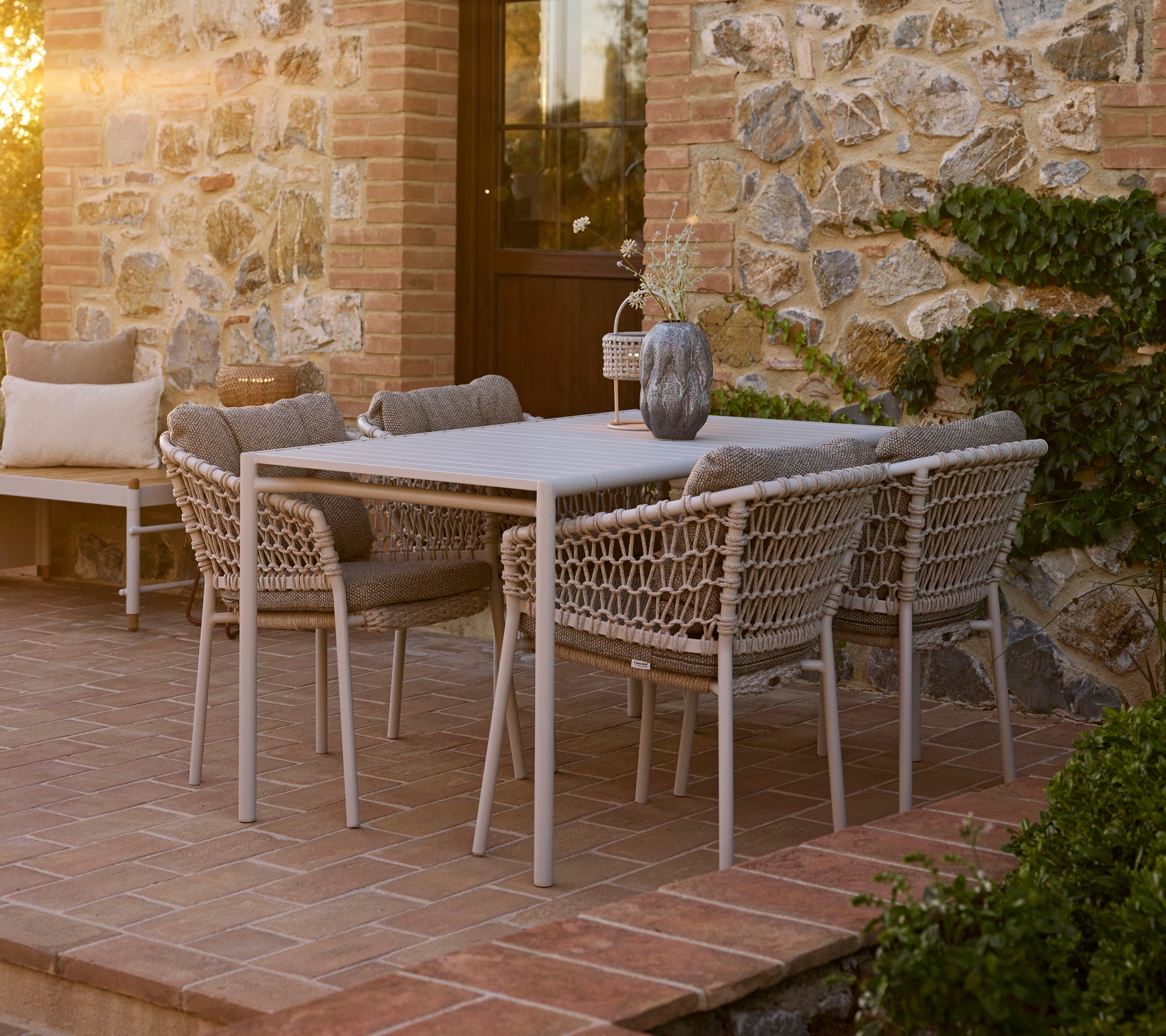 Strandachtige eetopstelling met een Bliss tafel omringd door Ocean eetstoelen, tegen een charmante stenen achtergrond.