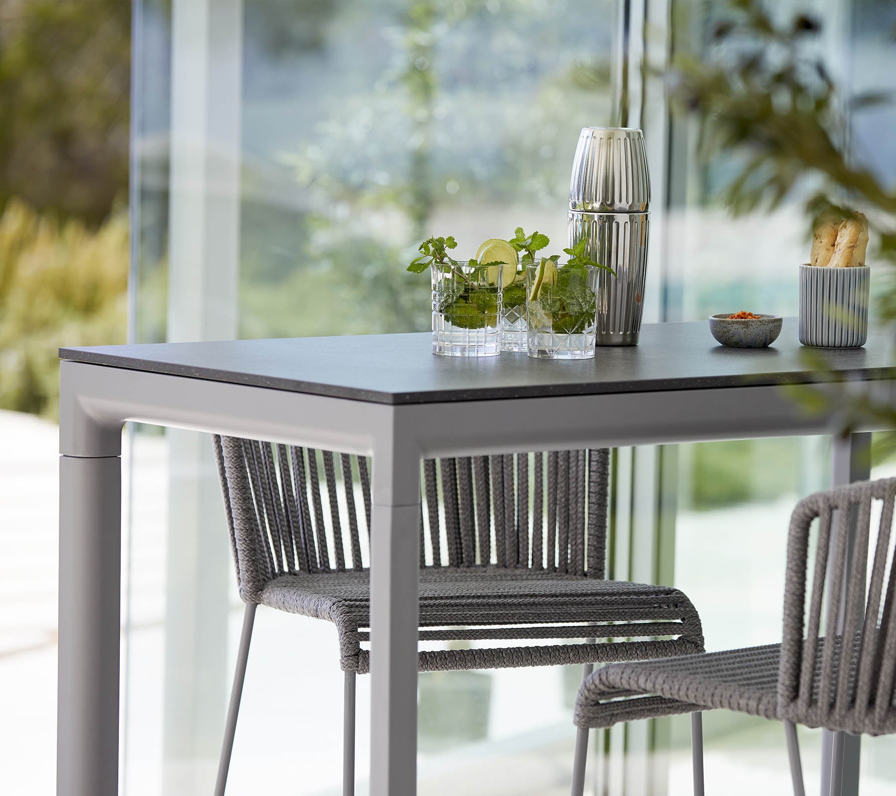 Een moderne tafel met twee stijlvolle stoelen, versierd met decoratieve planten en een klein schoteltje, tegen een heldere, open achtergrond.