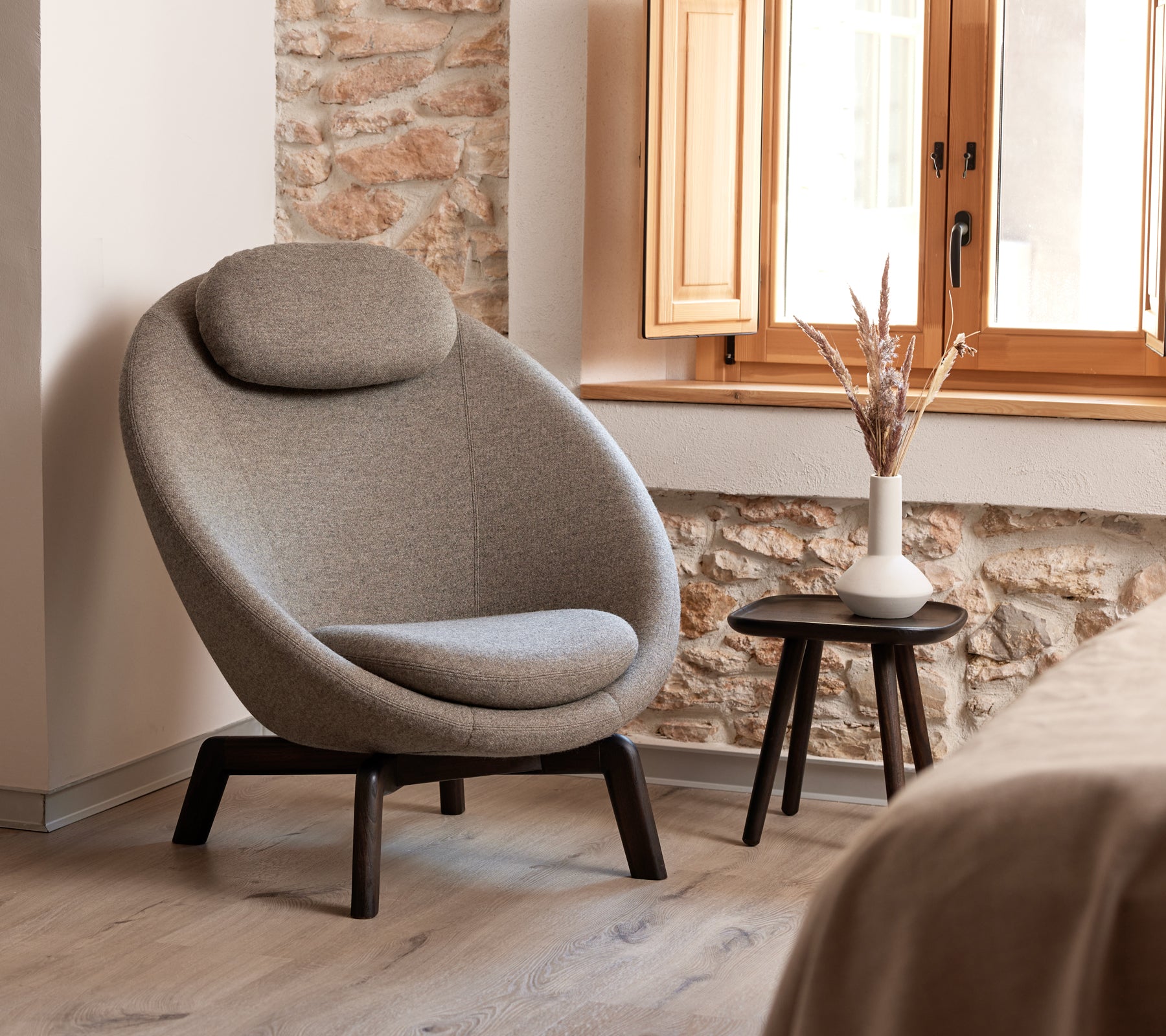 Stijlvolle, gebogen gestoffeerde stoel met een comfortabele hoofdsteun, vergezeld van een klein bijzettafeltje met een vaas en decoratieve elementen.