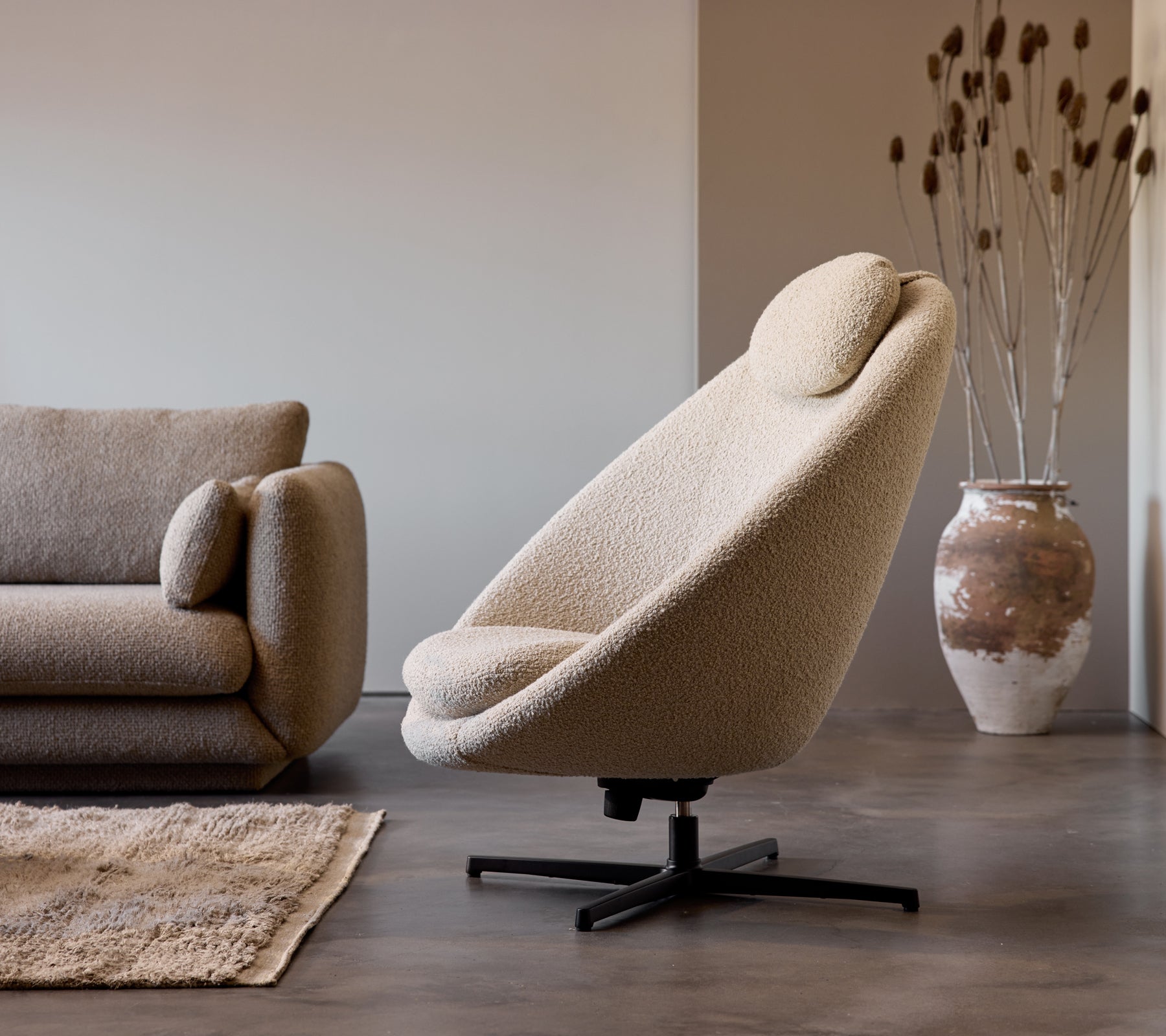 Pace stoel in taupe stof naast een Bloom 3-zitsbank, aangevuld met een decoratieve vaas en subtiele vloer textuur.