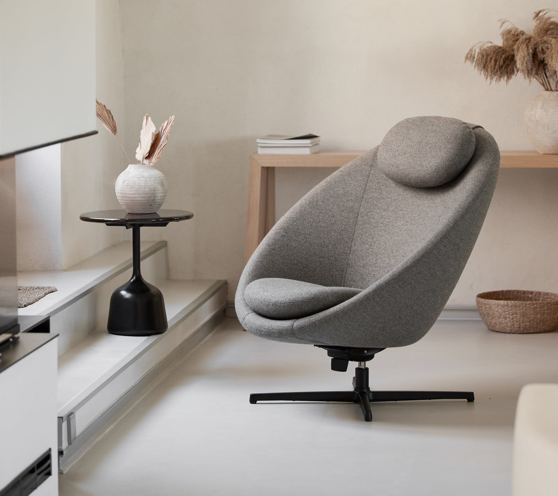 Stijlvolle grijze stoel met een gebogen vorm en ondersteunende hoofdsteun, aangevuld met een minimalistische salontafel en decoratieve elementen.