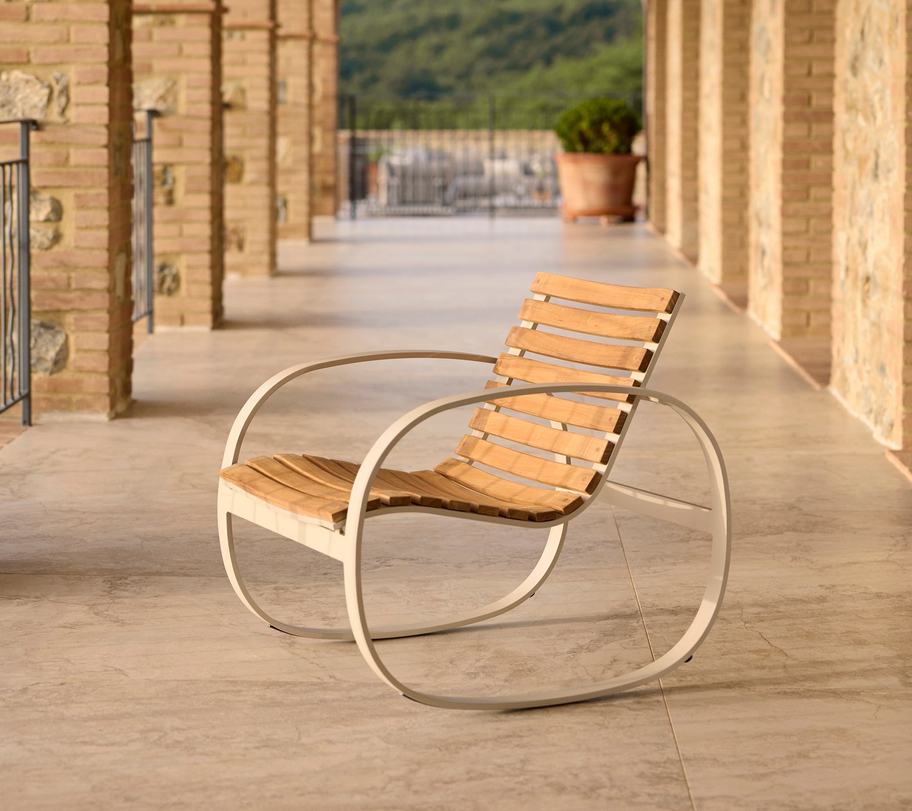 Parc schommelstoel met een aluminium frame en houten latten, gepositioneerd op een terras met stenen vloer en een schilderachtige achtergrond.