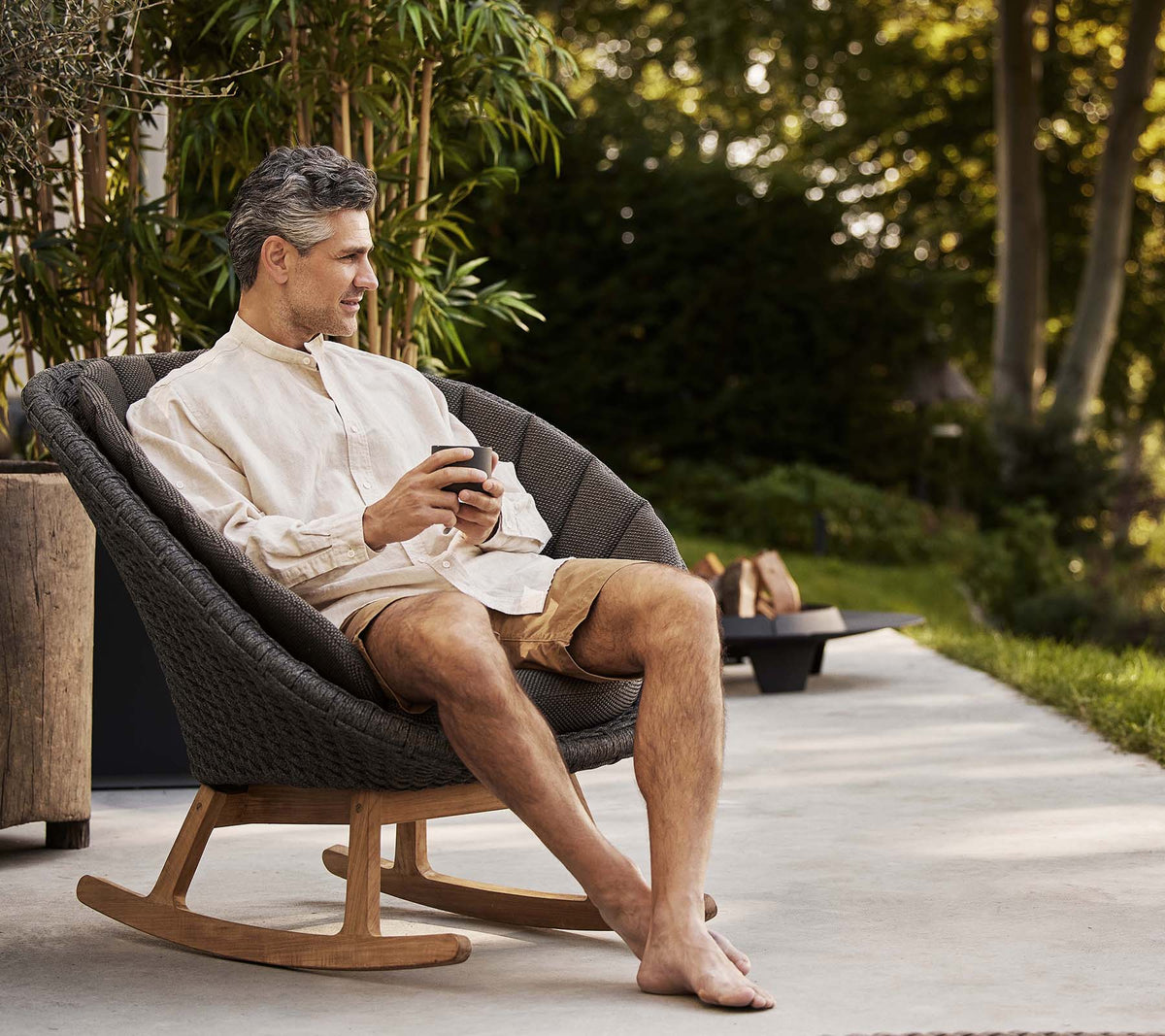 Een man zit comfortabel in een stijlvolle pauwen schommelstoel en geniet van een moment van ontspanning terwijl hij een telefoon vasthoudt. Groene planten zijn op de achtergrond.
