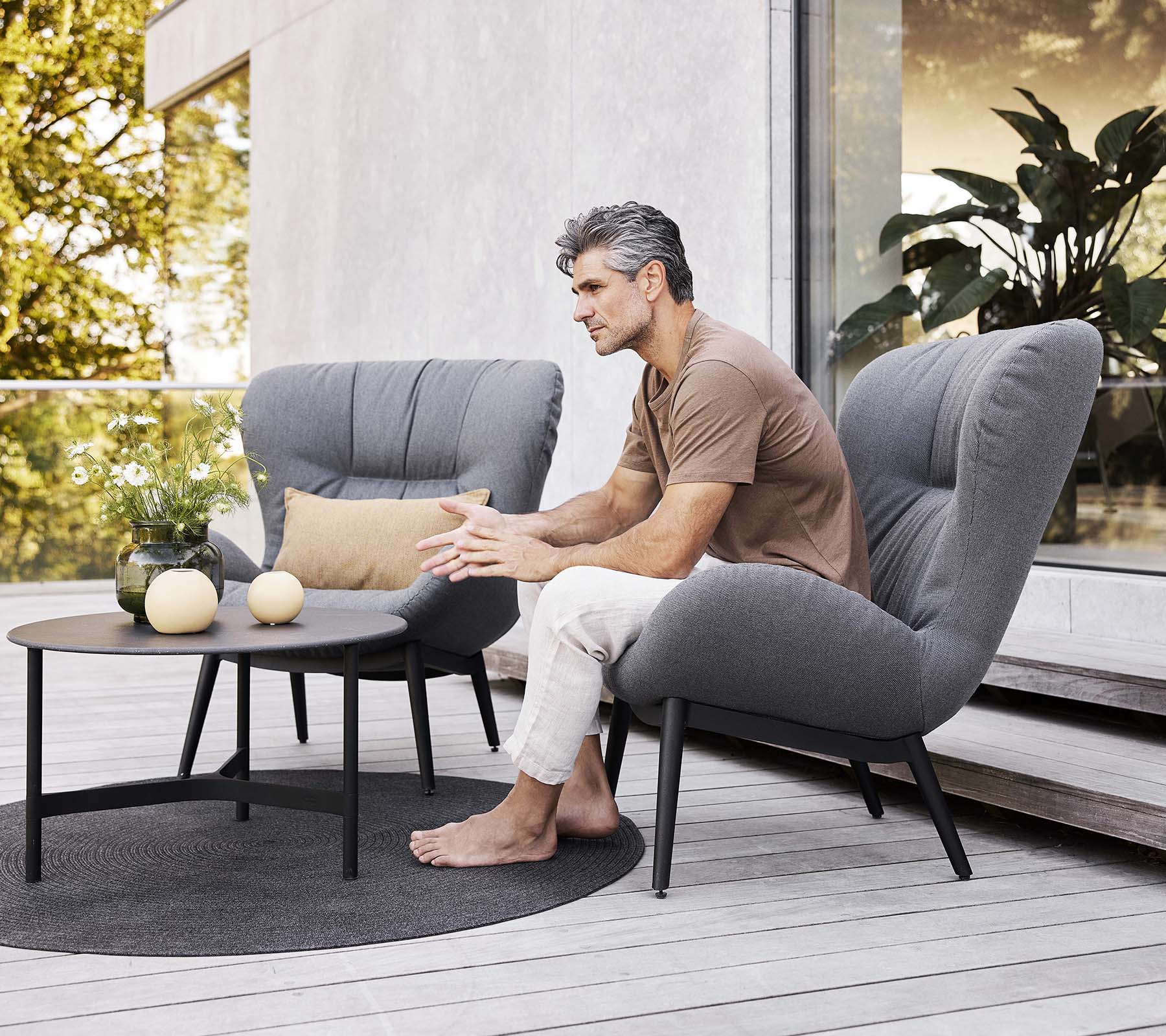 Een serene loungechair met een zittende man, een klein tafeltje in de buurt en decoratieve items, die een ontspannen sfeer creëren.