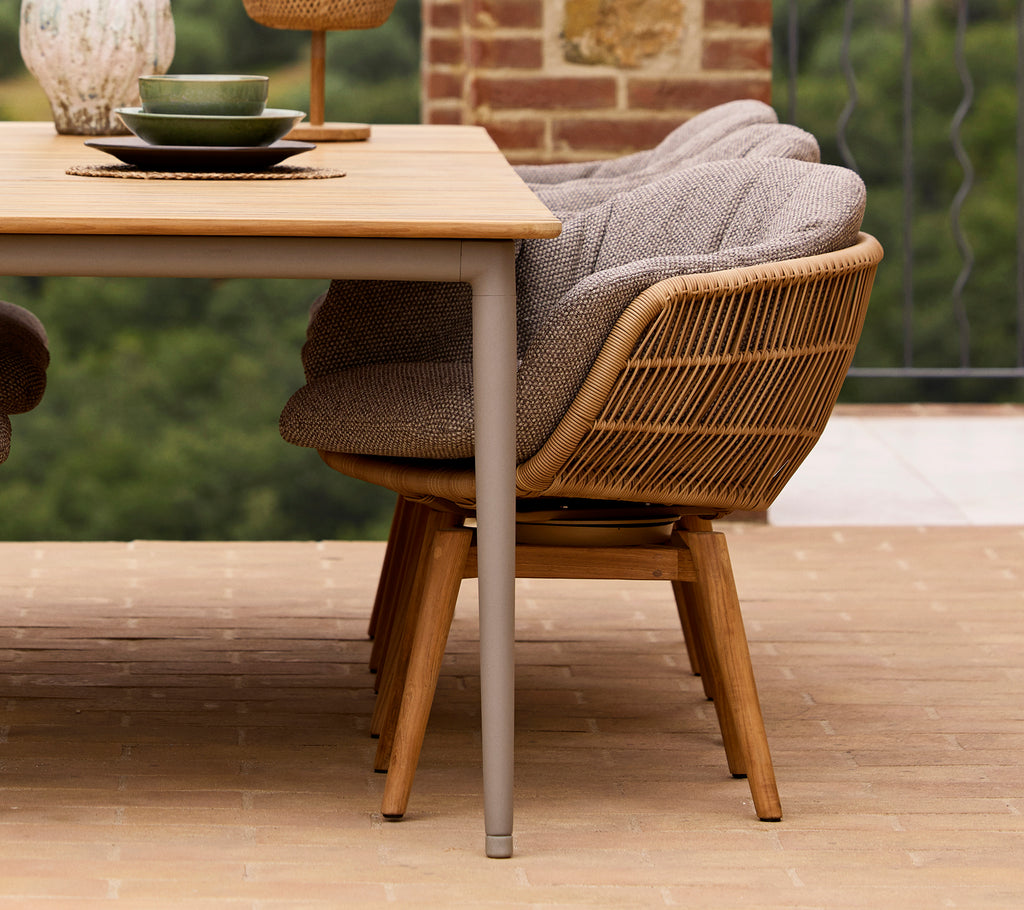 Stylish dining chair with a swivel design and teak legs, paired with a wooden table set elegantly for dining.