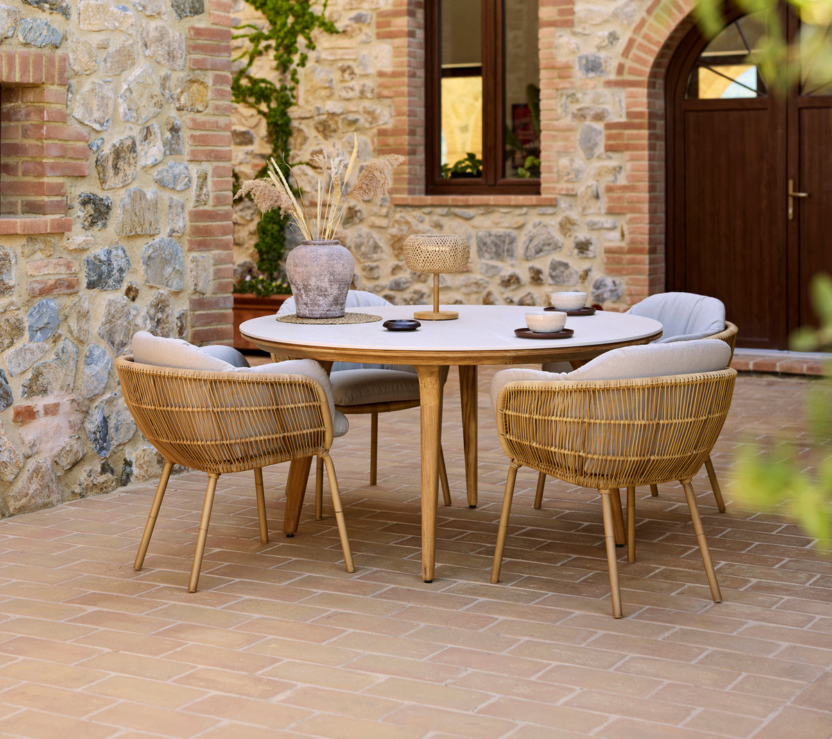 Buiten eetopstelling met een ronde Aspect tafel en Stay stoelen, tegen een stenen muur als achtergrond.