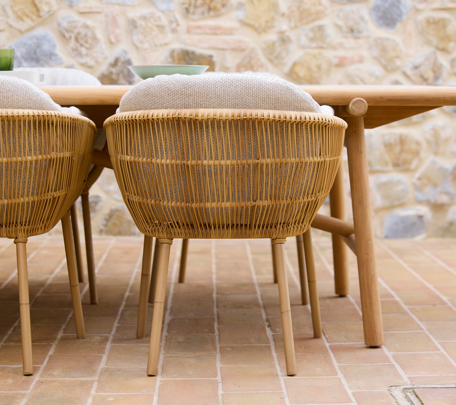 Twee geweven eetstoelen met aluminium poten, geplaatst naast een houten eettafel met een natuurlijke esthetiek.