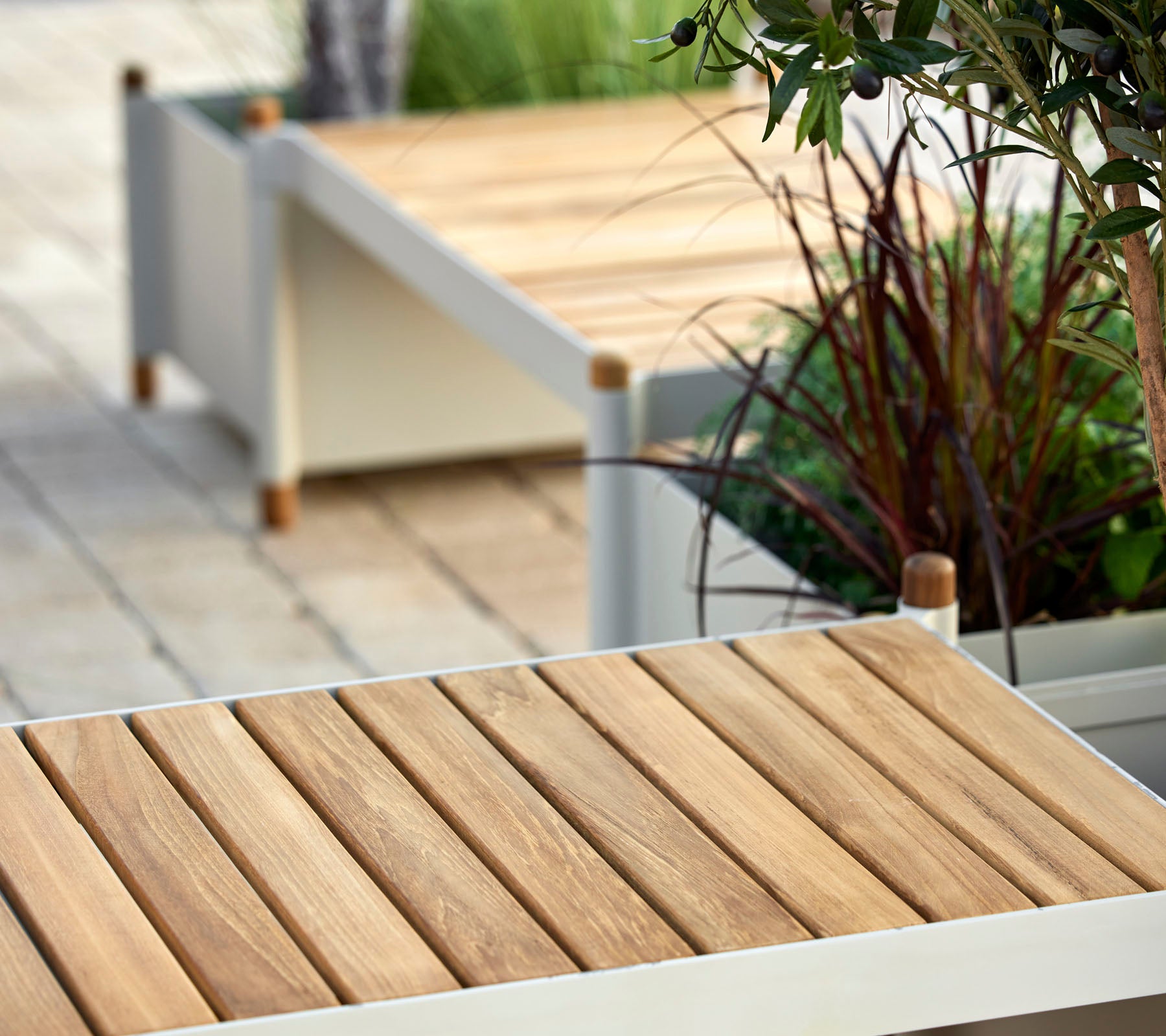 Houten lattenoppervlak met minimalistische designelementen, omringd door groen en decoratieve plantenbakken.