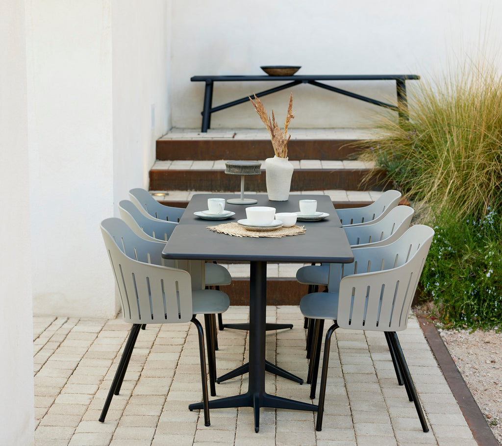 Een stijlvolle tafelset met zes lavagrijze stoelen, met een complementaire aluminium bank en decoratieve elementen zoals vazen en schalen.
