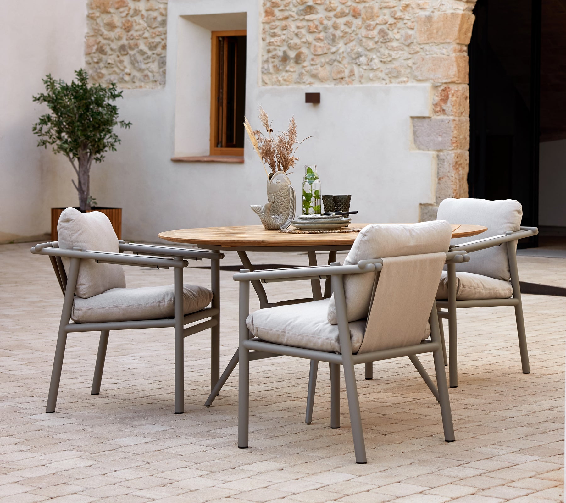 Modern eettafel met een houten bovenblad en aluminium frames, vergezeld van zachte, gestoffeerde stoelen, tegen een gestructureerde achtergrond.