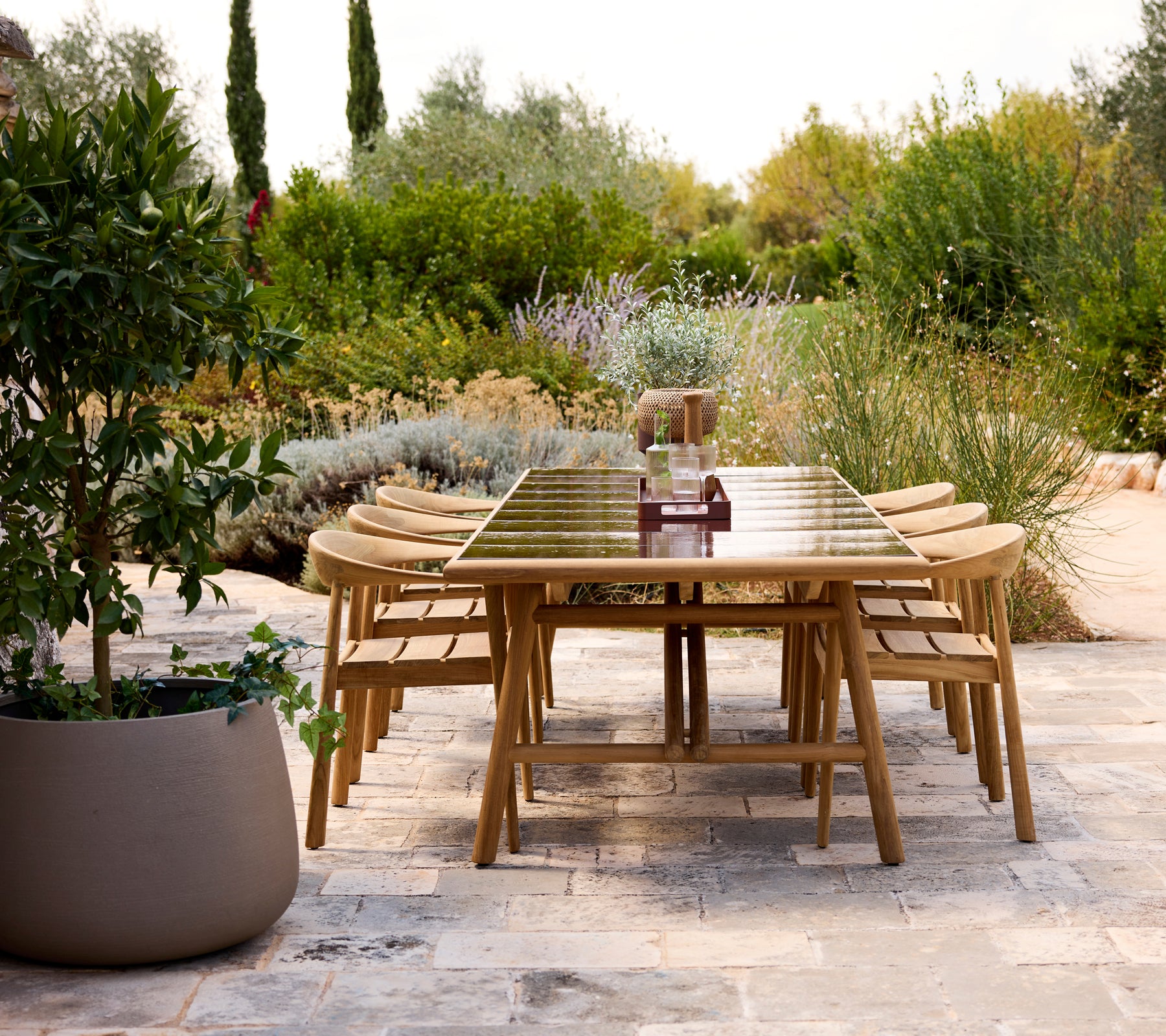Modern buitentafel met houten stoelen in een tuinsetting.