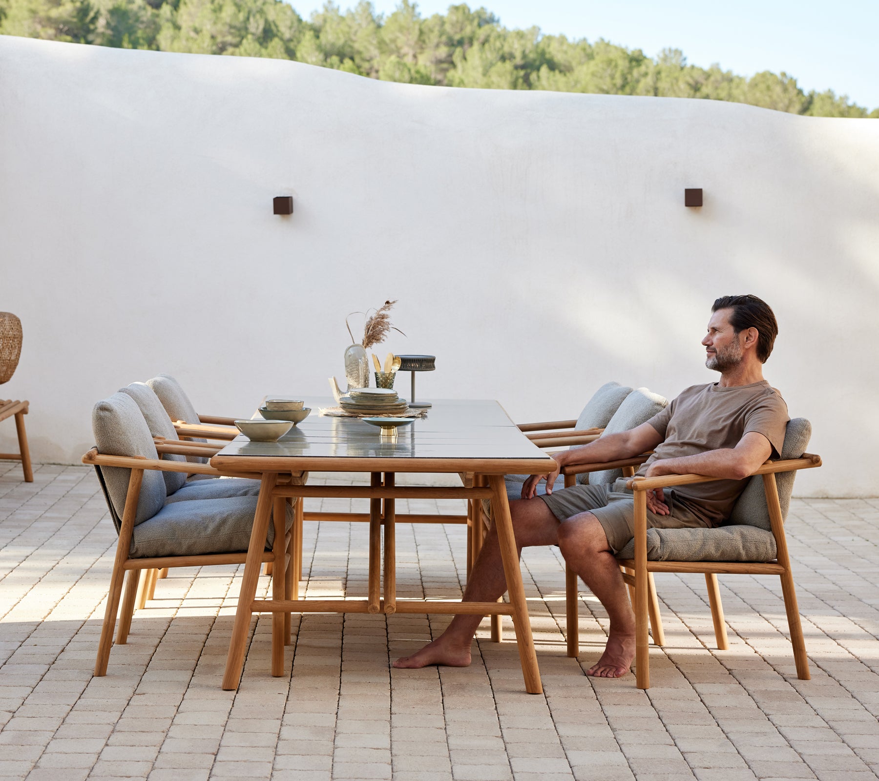 Een teak eetsetup met een lange tafel en comfortabele stoelen, met een persoon die zit en een ontspannen eet sfeer creëert.