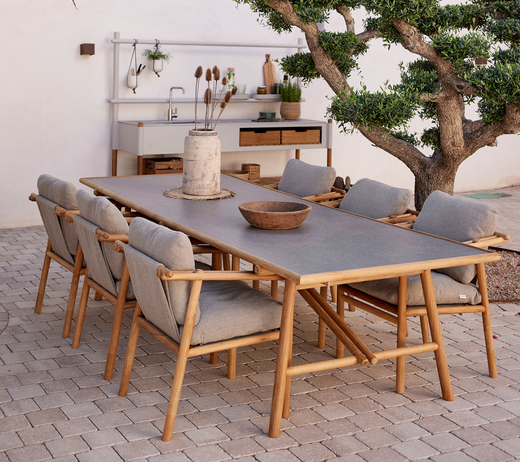 Teaken eettafel omringd door comfortabele stoelen, met natuurlijke elementen en een minimalistische decorstijl.