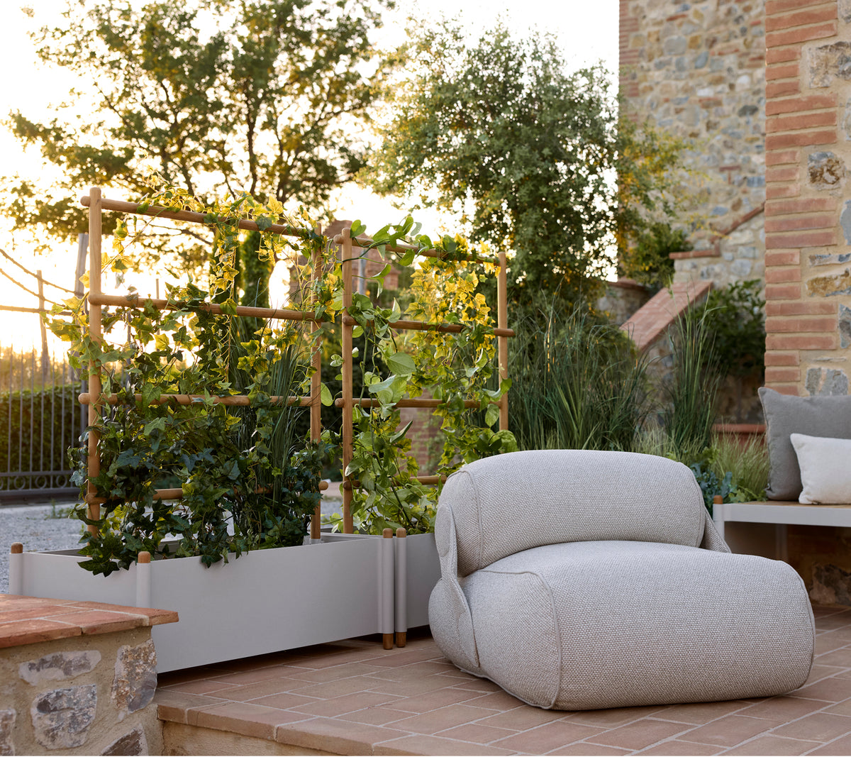 Zachte lounge stoel naast een stijlvolle planter, met groenblijvende planten en een serene buitenomgeving met warm natuurlijk licht.