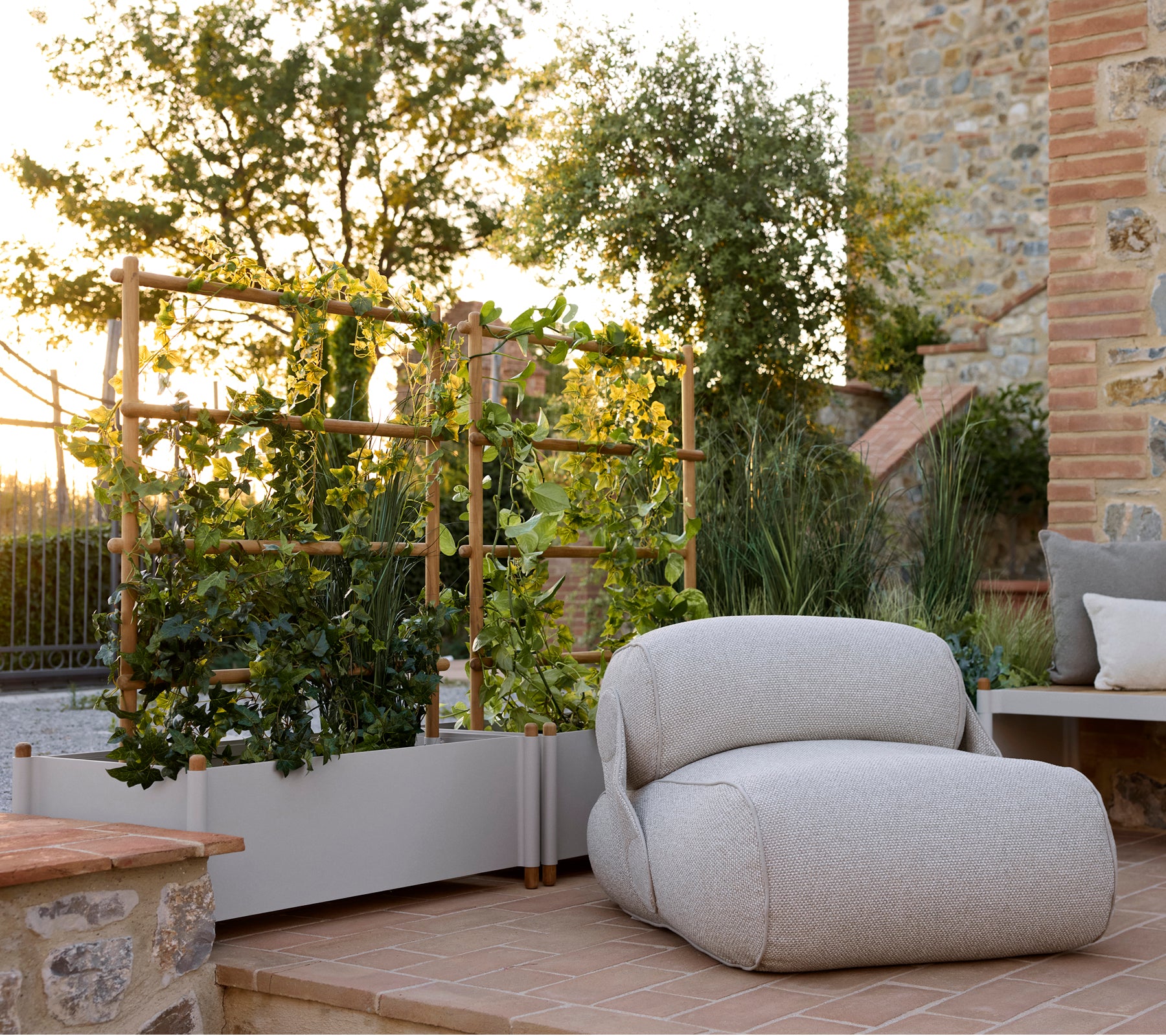 Zachte lounge stoel naast een stijlvolle planter, met groenblijvende planten en een serene buitenomgeving met warm natuurlijk licht.