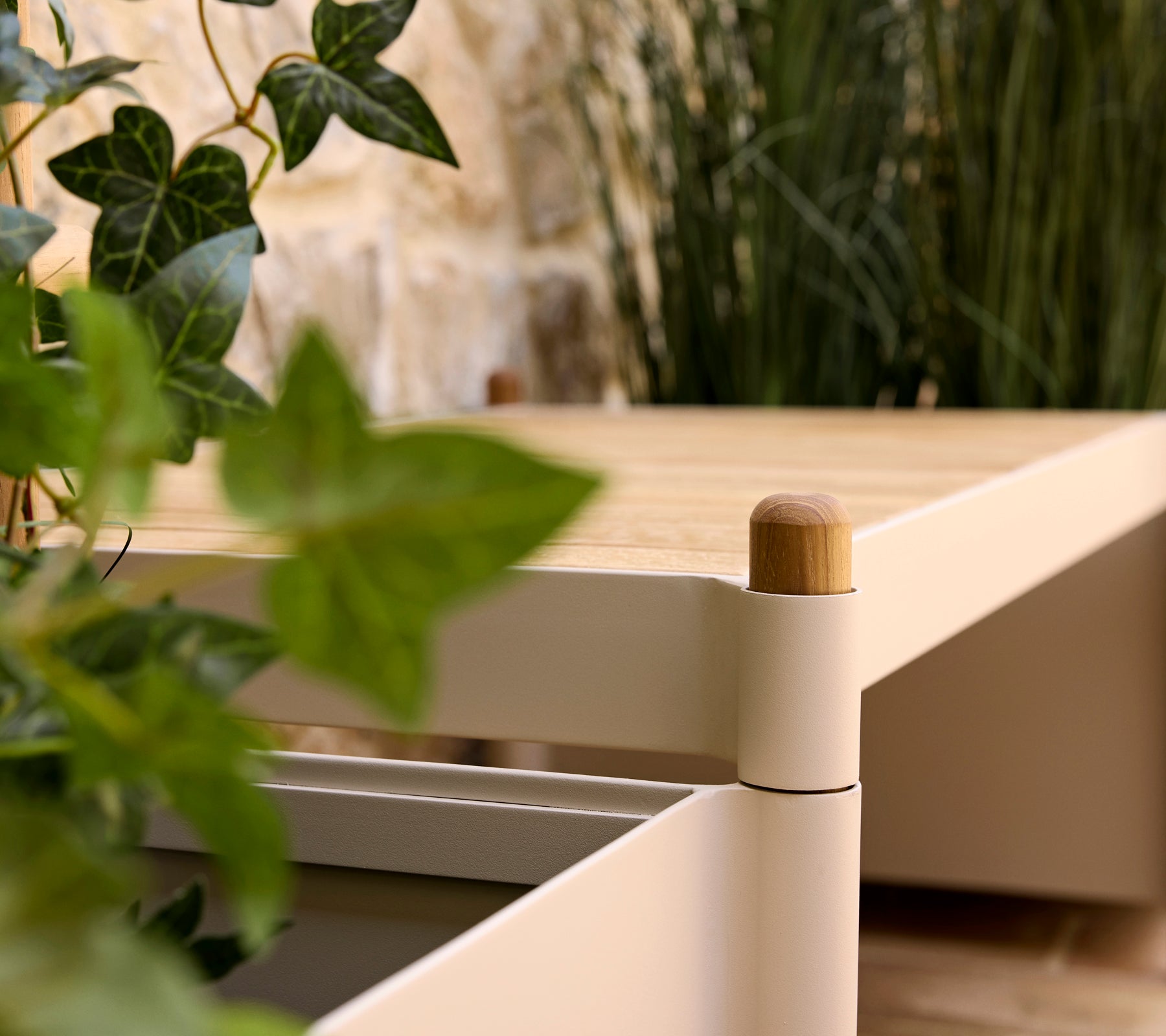 Een stijlvolle bank met een houten top en ronde hoeken, vergezeld door groen in een plantenbak, wat een serene sfeer bevordert.
