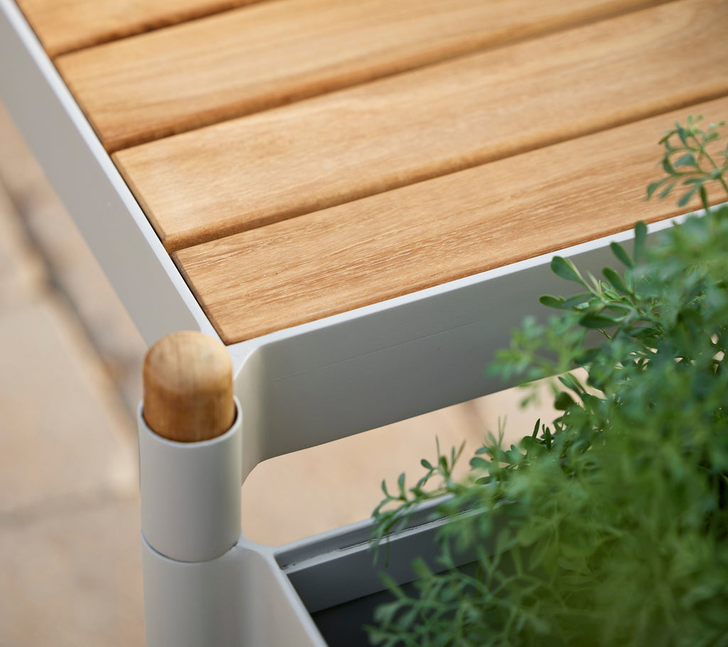 Bank met teaklattenblad, een wit frame en groene planten, met een ronde houten stokdetail.