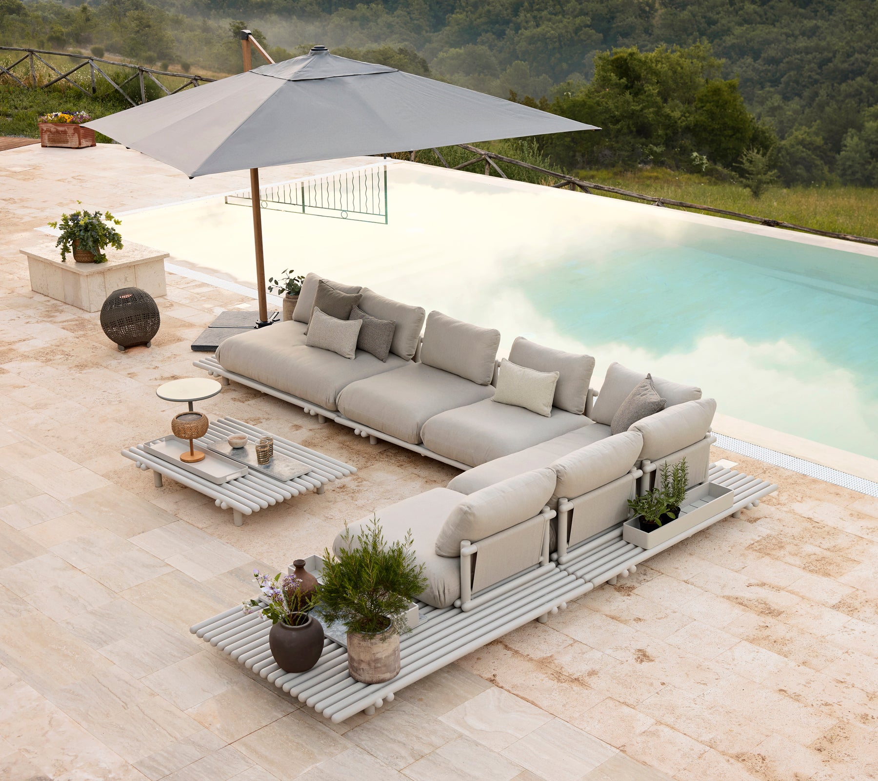 Stijlvolle aluminium lounge set met plush kussens en een bijpassende salontafel, aangevuld met een parasol en decoratieve planten.