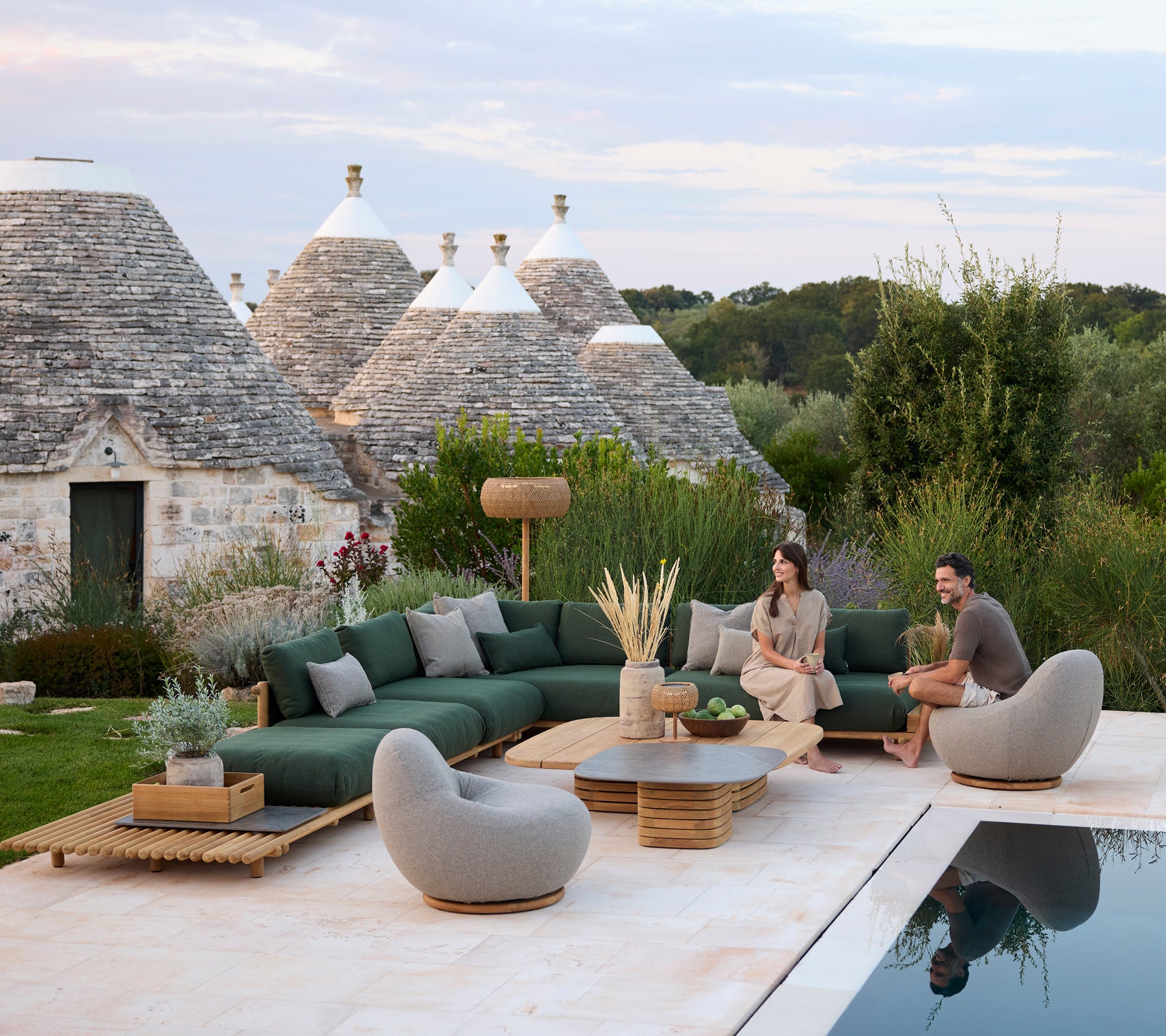 Moderne buiten loungegedeelte met groene sectie-sofa en grijze stoelen bij een zwembad.