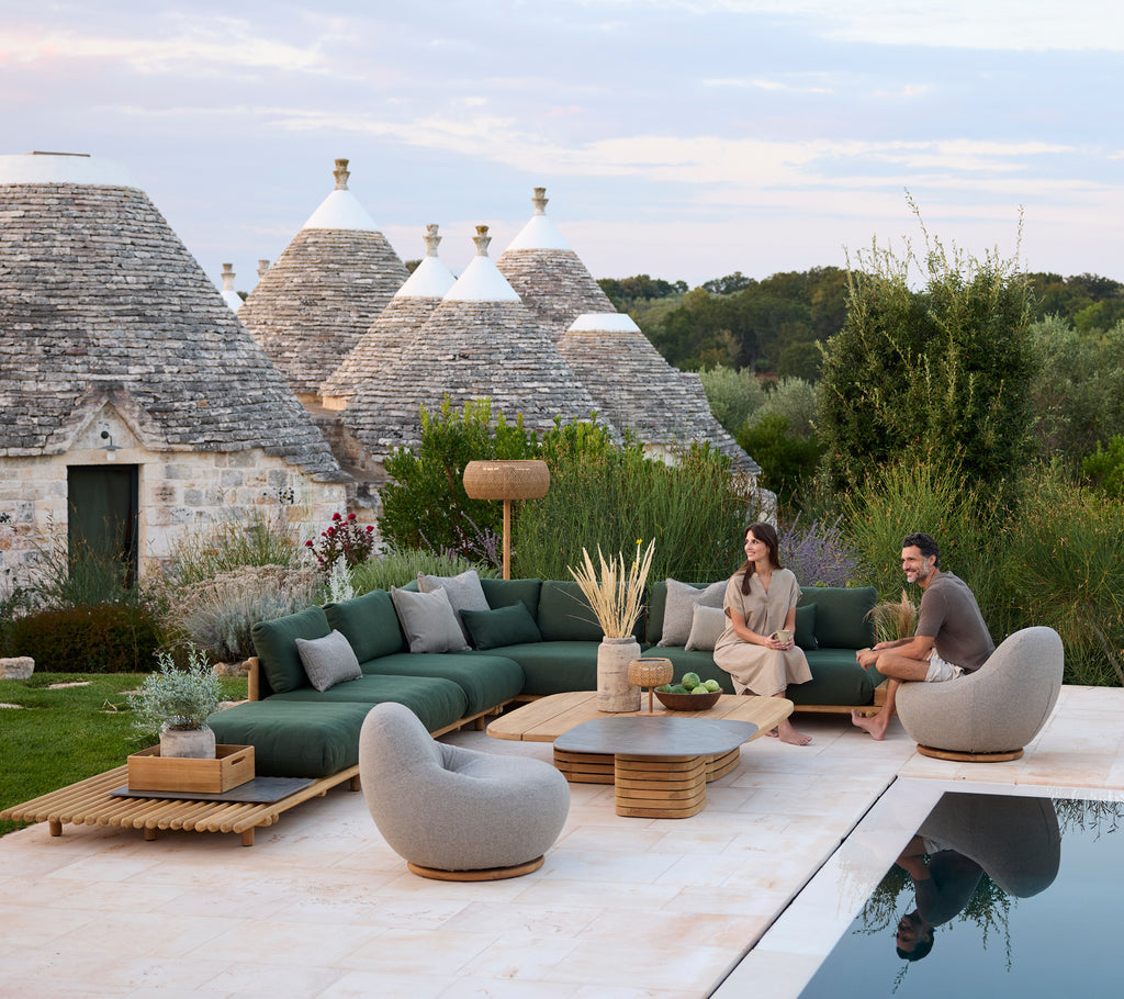 Moderne buiten loungegedeelte met groene sectie-sofa en grijze stoelen bij een zwembad.