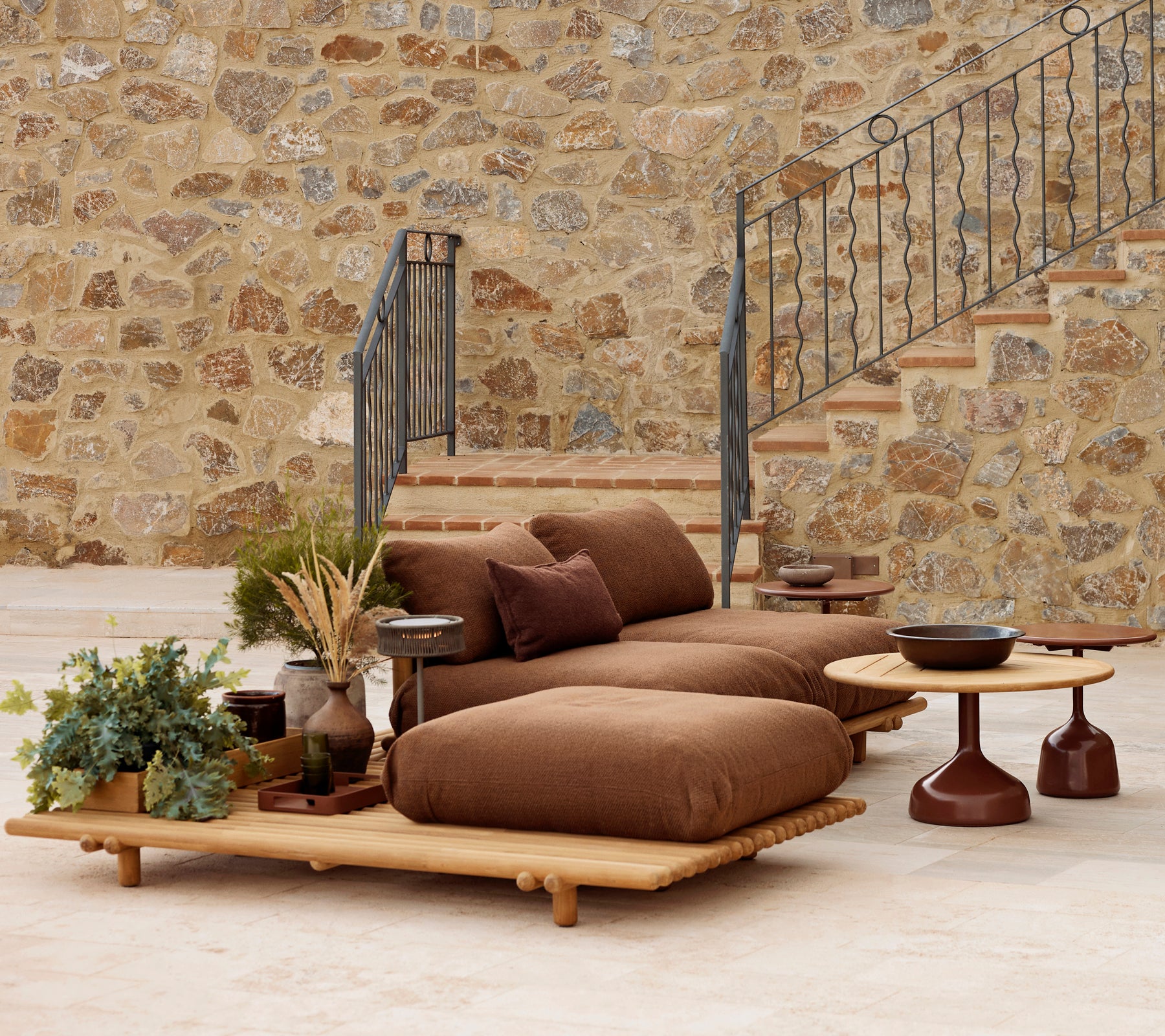 Teak-lounge met pluche kussens en een Glaze salontafel, aangevuld met decoratieve planten en een gestructureerde stenen achtergrond.