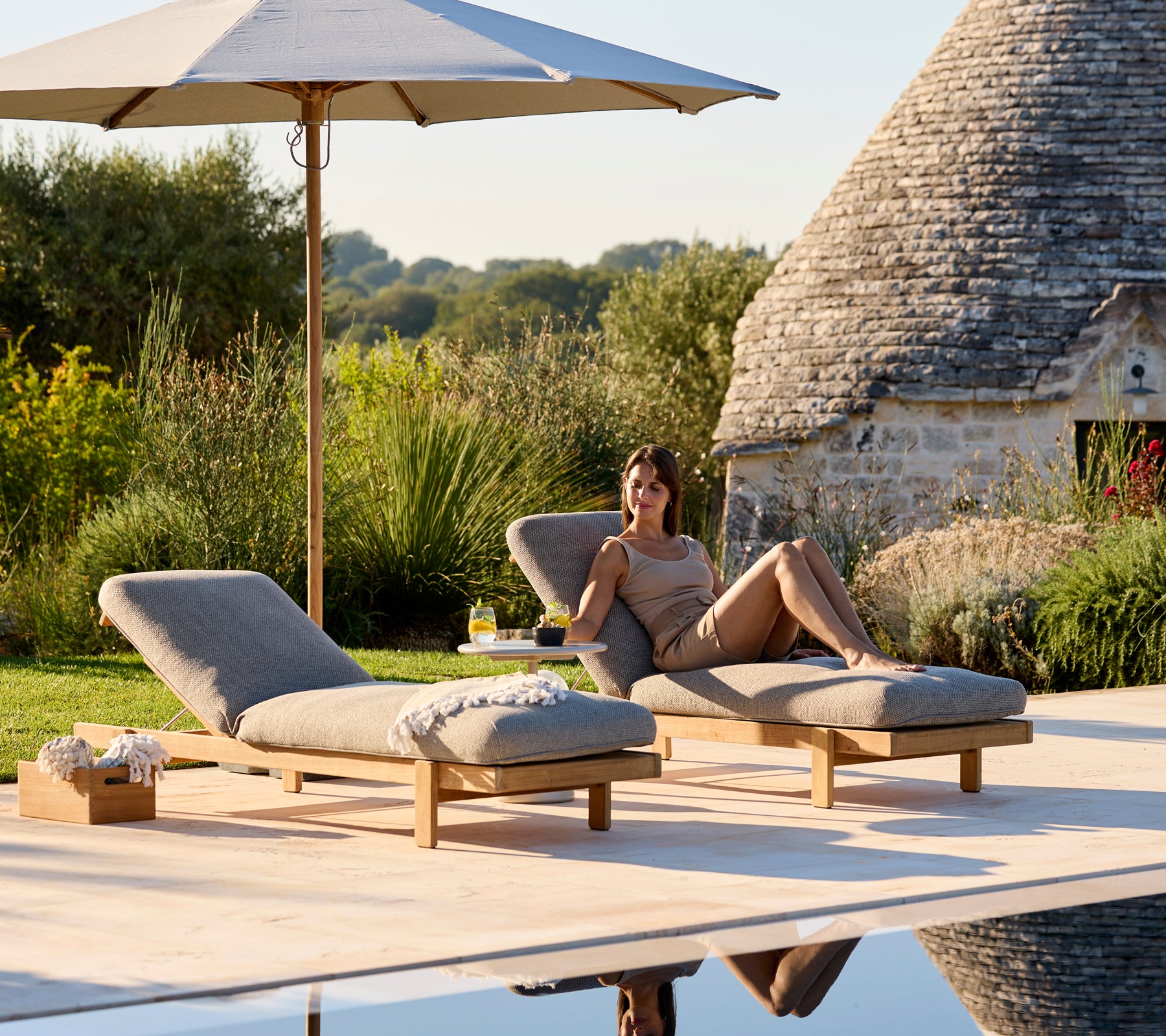 Twee ligstoelen met beige kussens onder een parasol in een serene buitenomgeving.