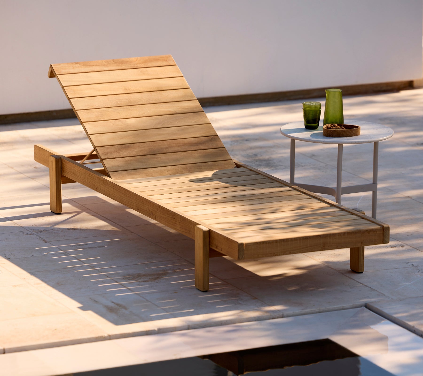 Houten ligstoel met een witte bijzettafel in een moderne buitenomgeving.