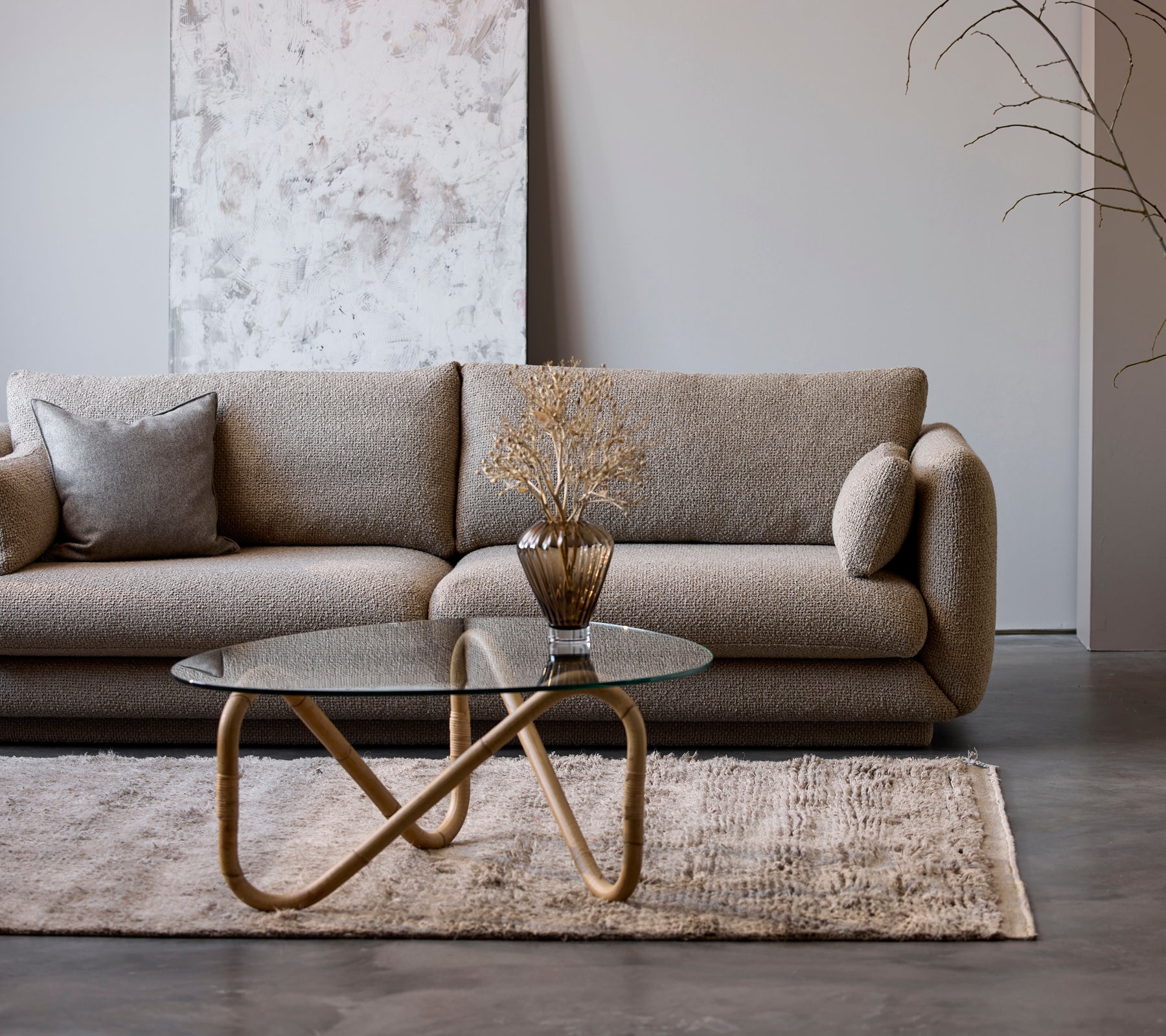 Een moderne beige bank met een glazen salontafel en een decoratieve vaas in een minimalistische lounge-setting.