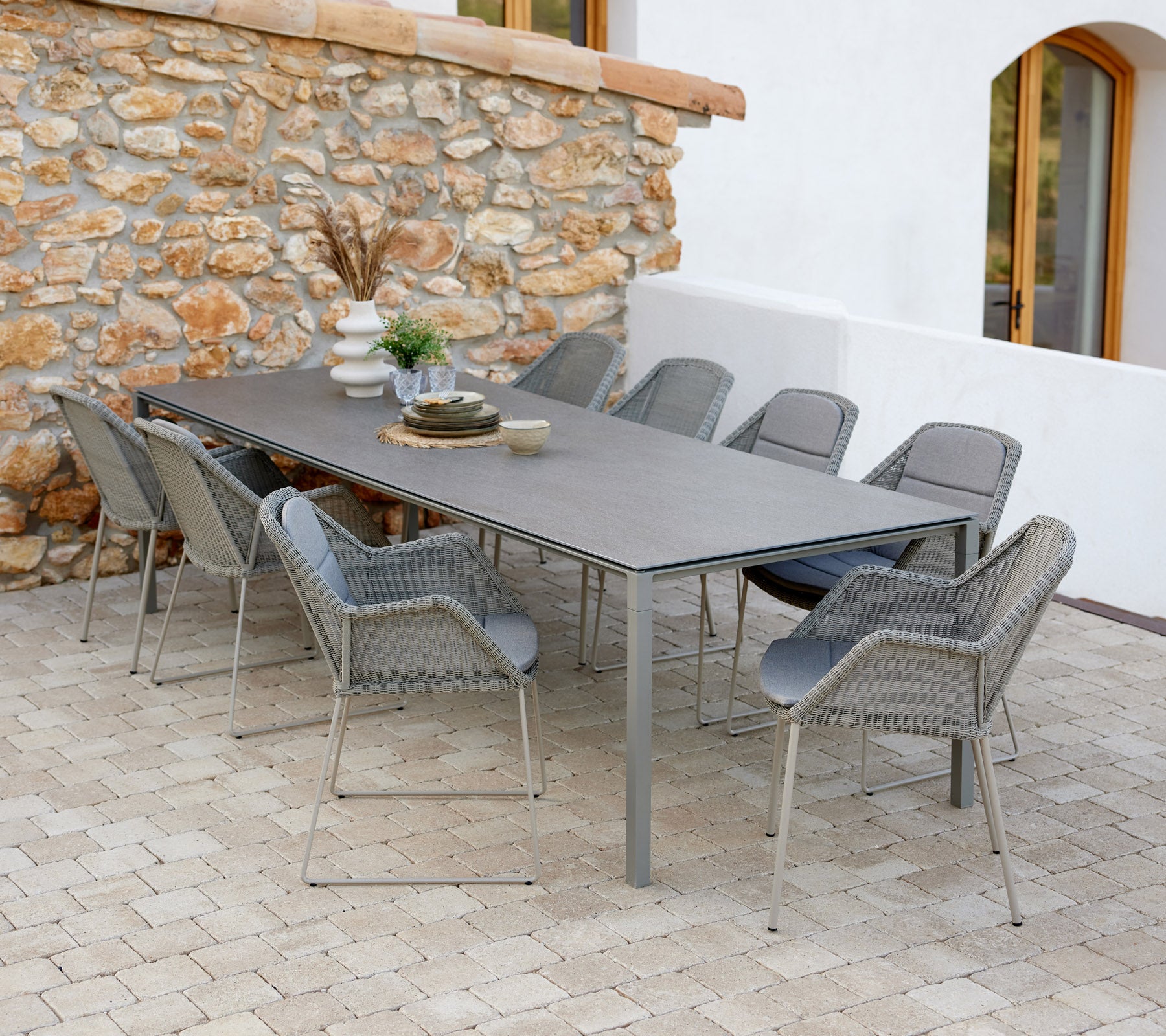 Moderne eettafel met taupe stoelen, gezet met decoratieve items en een vleugje groen tegen een stenen muur.
